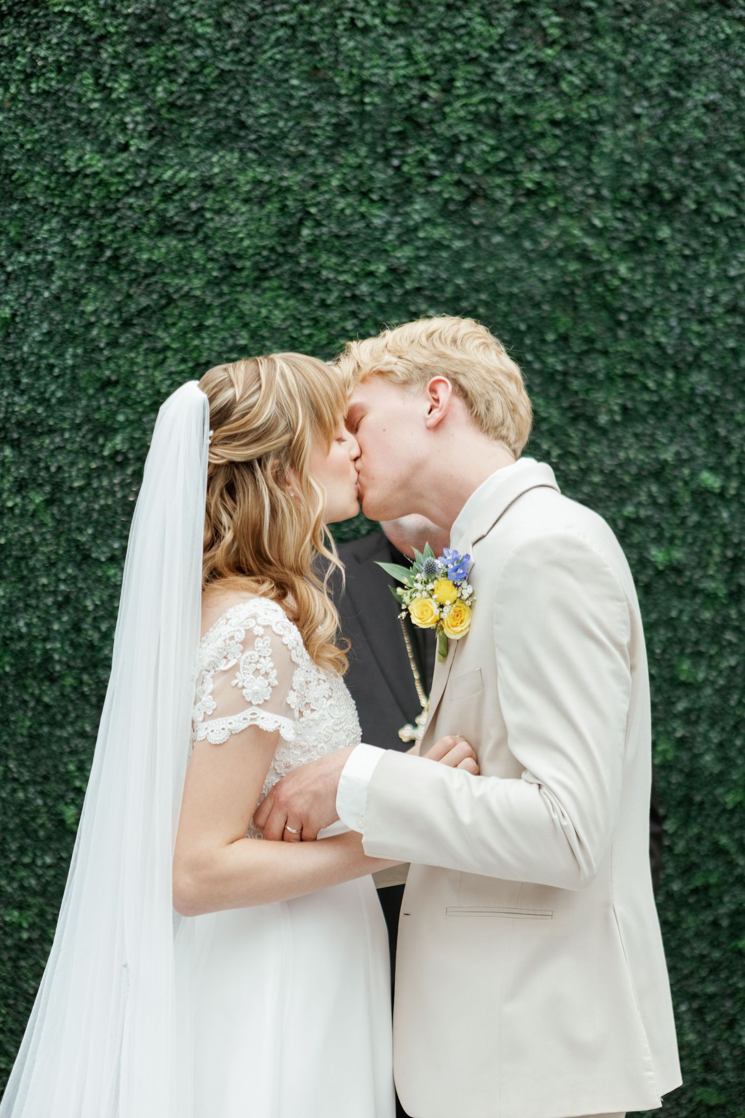 Romantic wedding ceremony moment captured against lush green hedge backdrop.