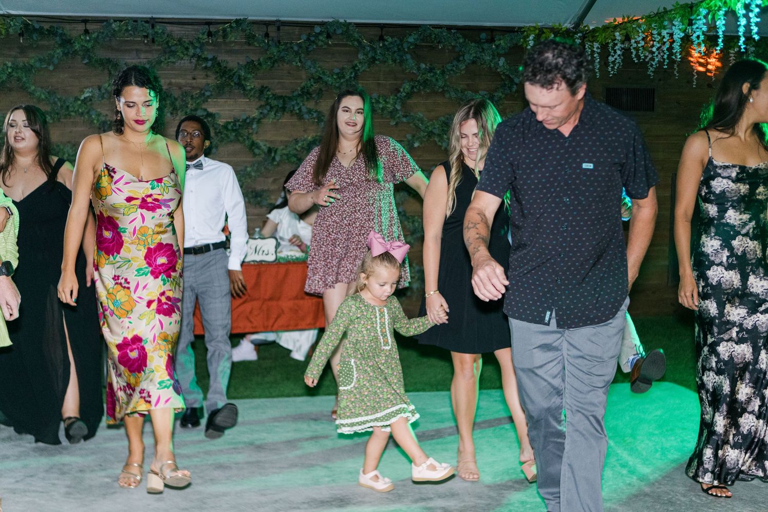 Lively wedding reception with guests dancing under green lighting and decorative elements.