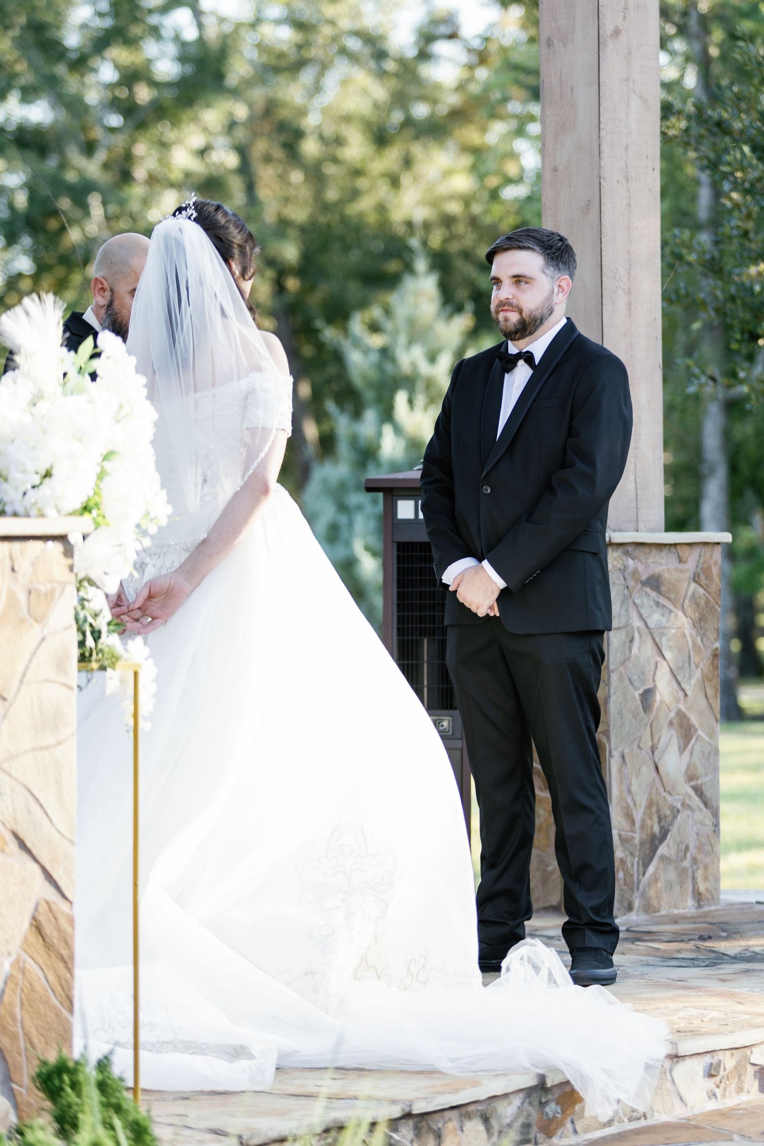 Wedding ceremony moments captured under a stone pillar pavilion with flowing white dress.