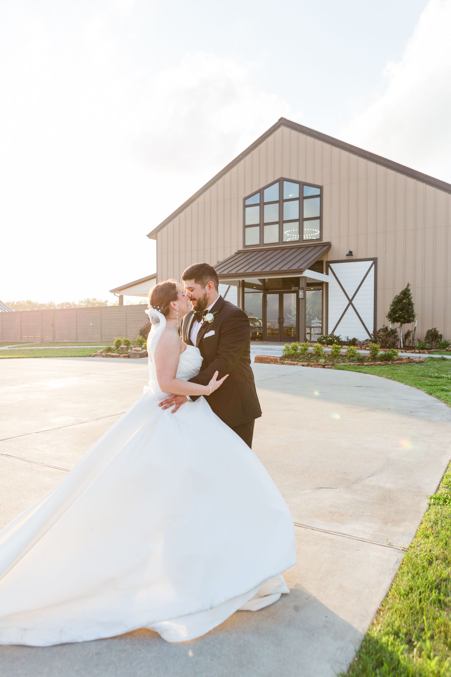 Wedding couple dancing outside modern barn venue at sunset.