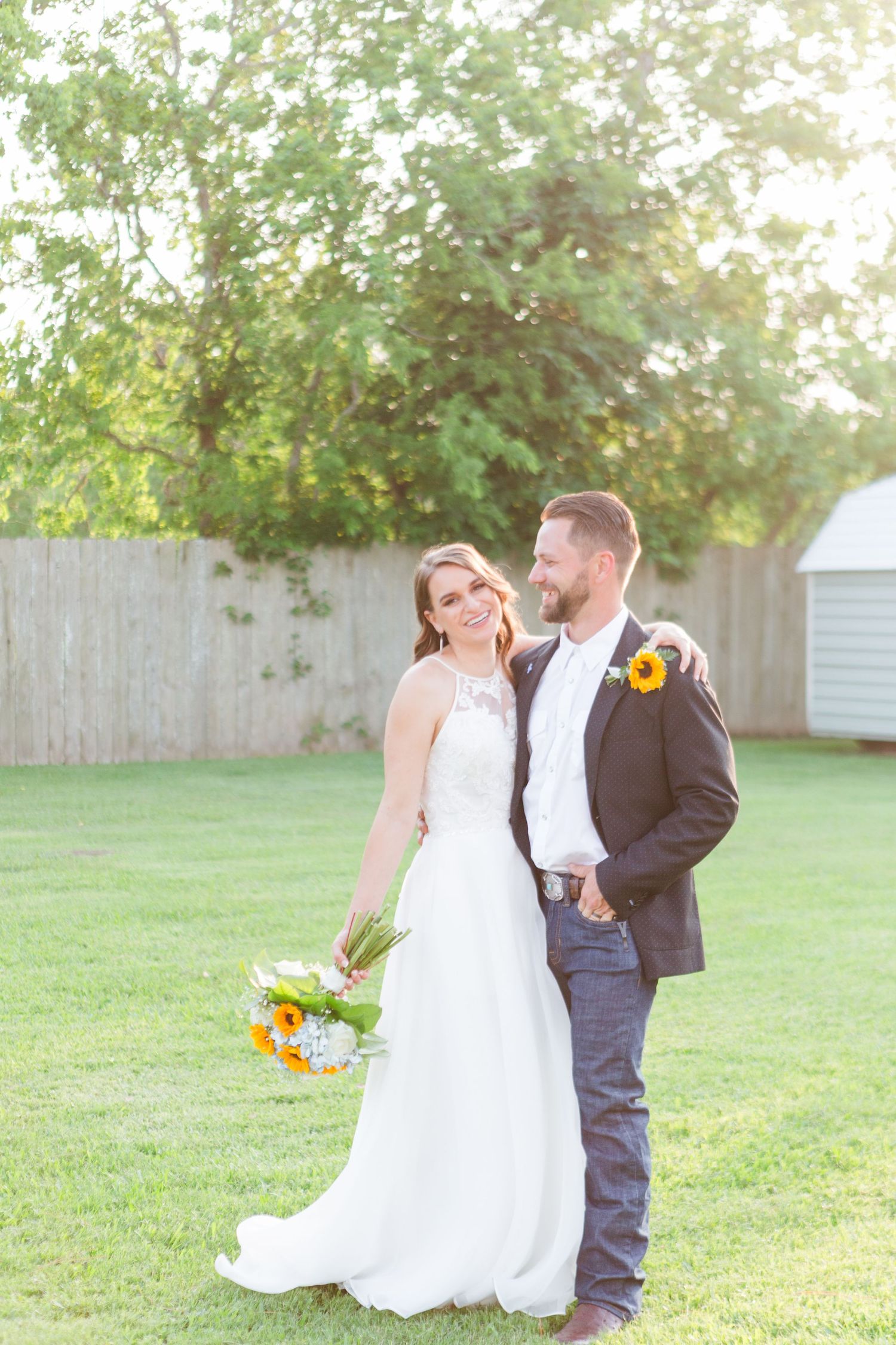 Sunlit wedding photos on green lawn with white dress and sunflower bouquet.