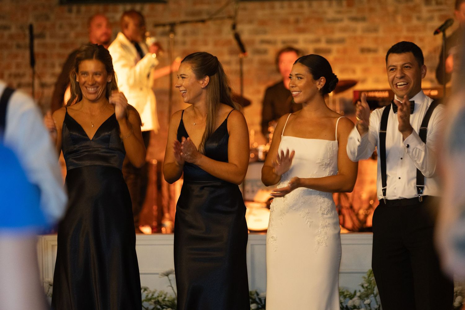 Wedding reception guests celebrate on dance floor with exposed brick walls and warm lighting.