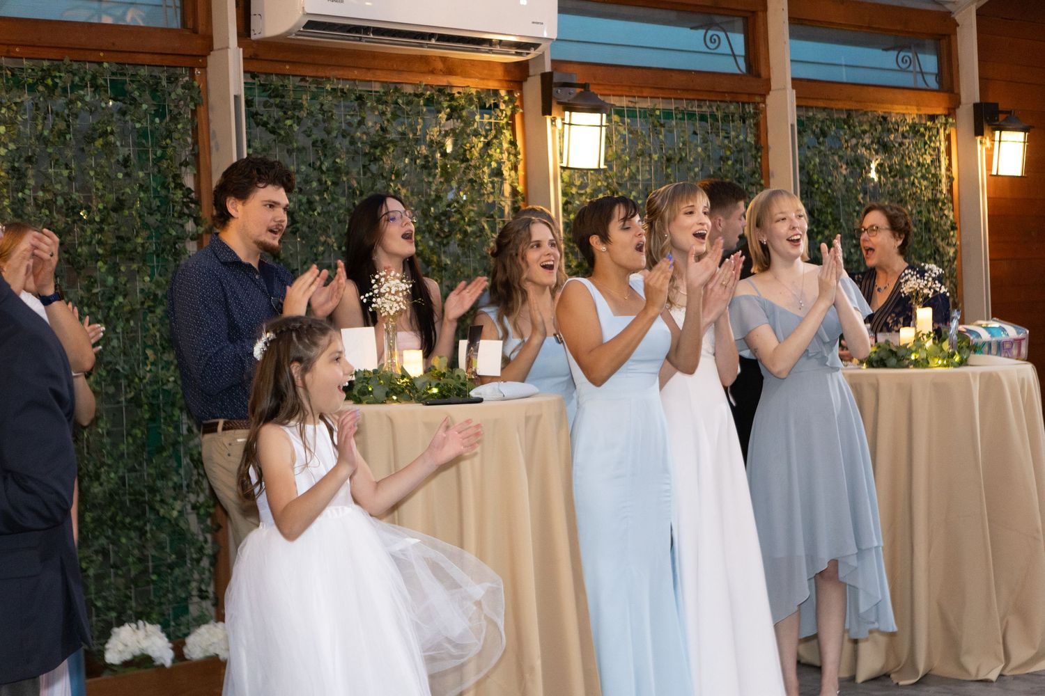Wedding reception guests gathered in formal attire under wooden beams and natural lighting.
