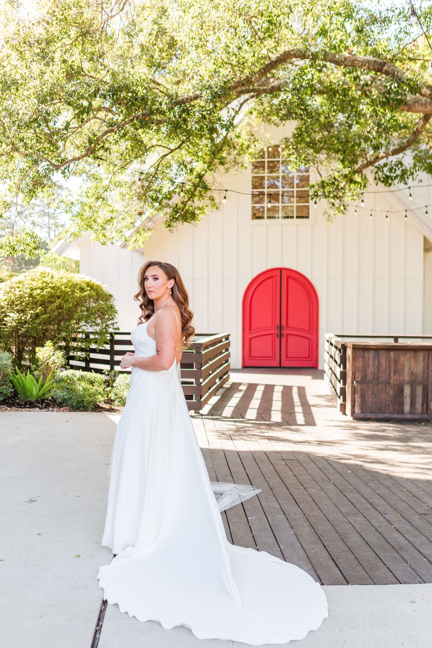 Elegant wedding dress with train shown against white building with red door backdrop.