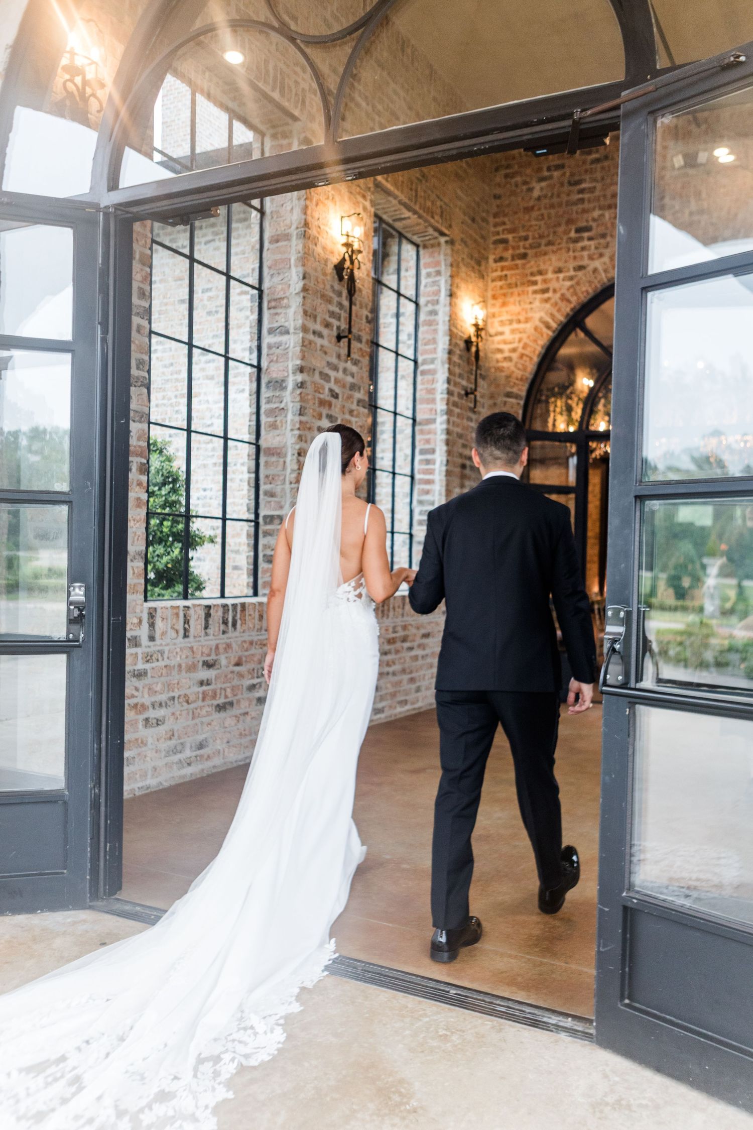 Wedding couple walking through an elegant brick venue with large glass doors.