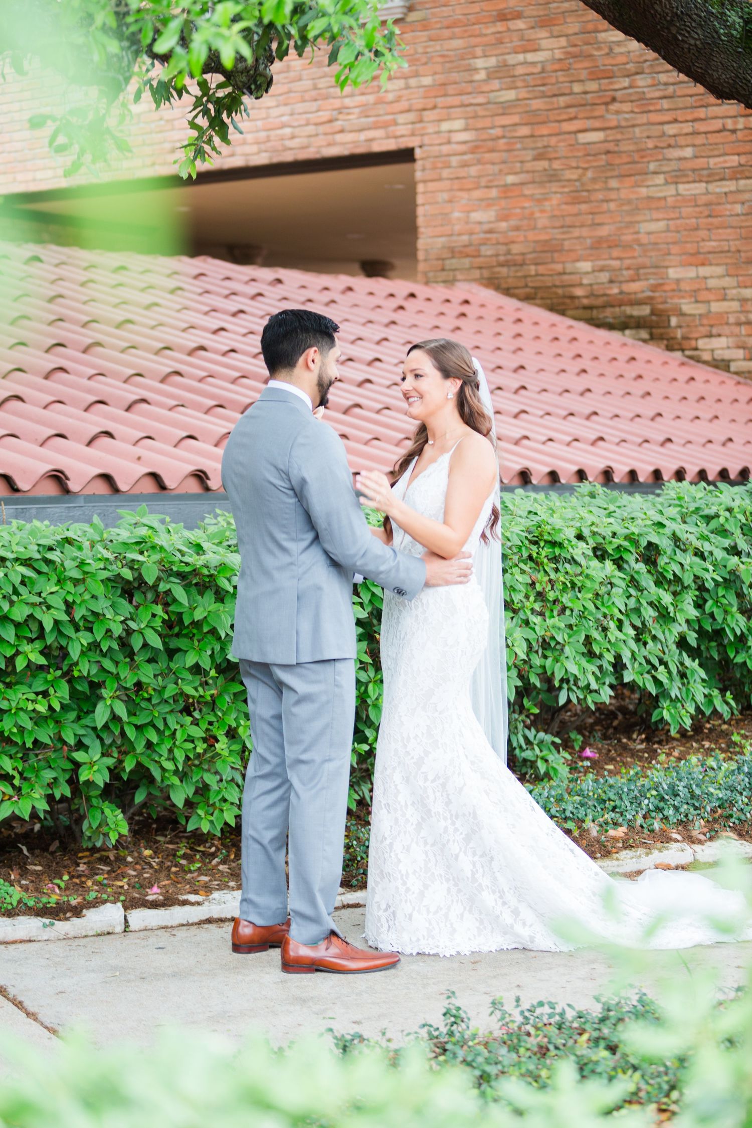 Wedding couple sharing special moment by brick wall with lush greenery.