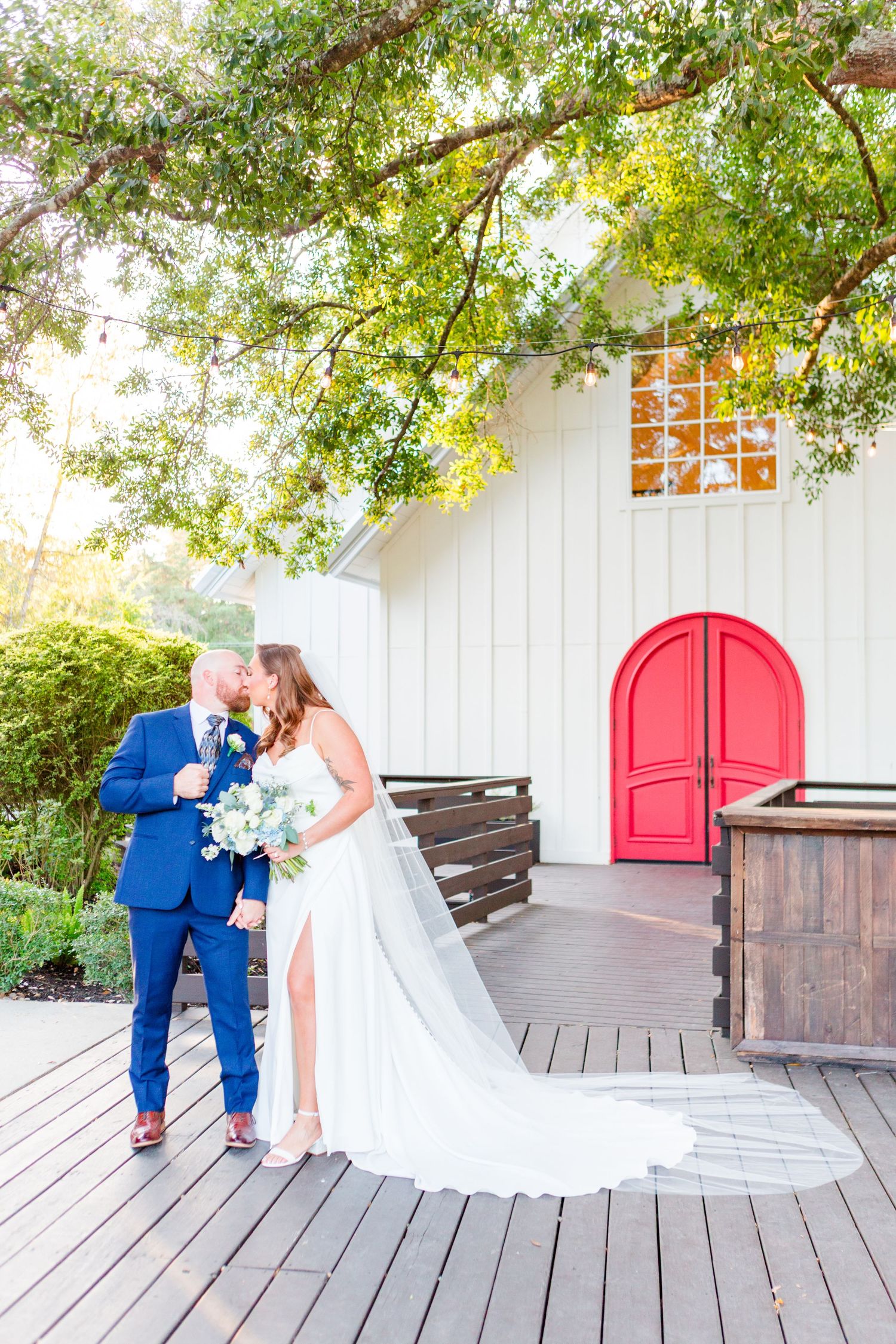 Wedding ceremony venue with white walls, red doors and wooden deck under shady trees.