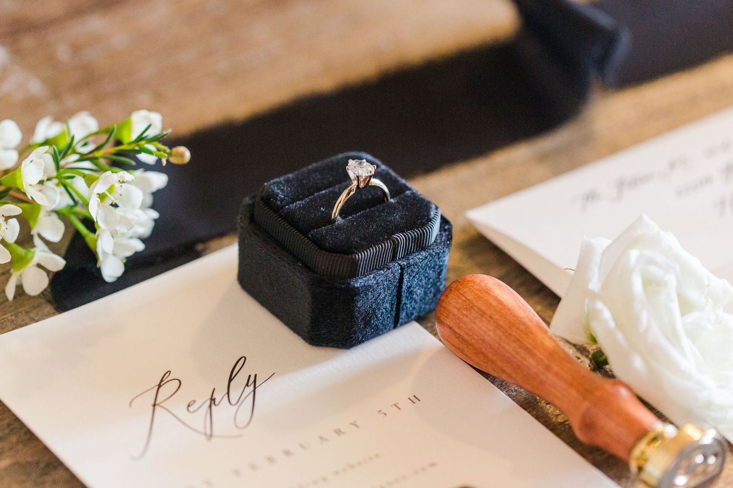 Black and white wedding stationery with wooden wax seal stamp and delicate floral accents.