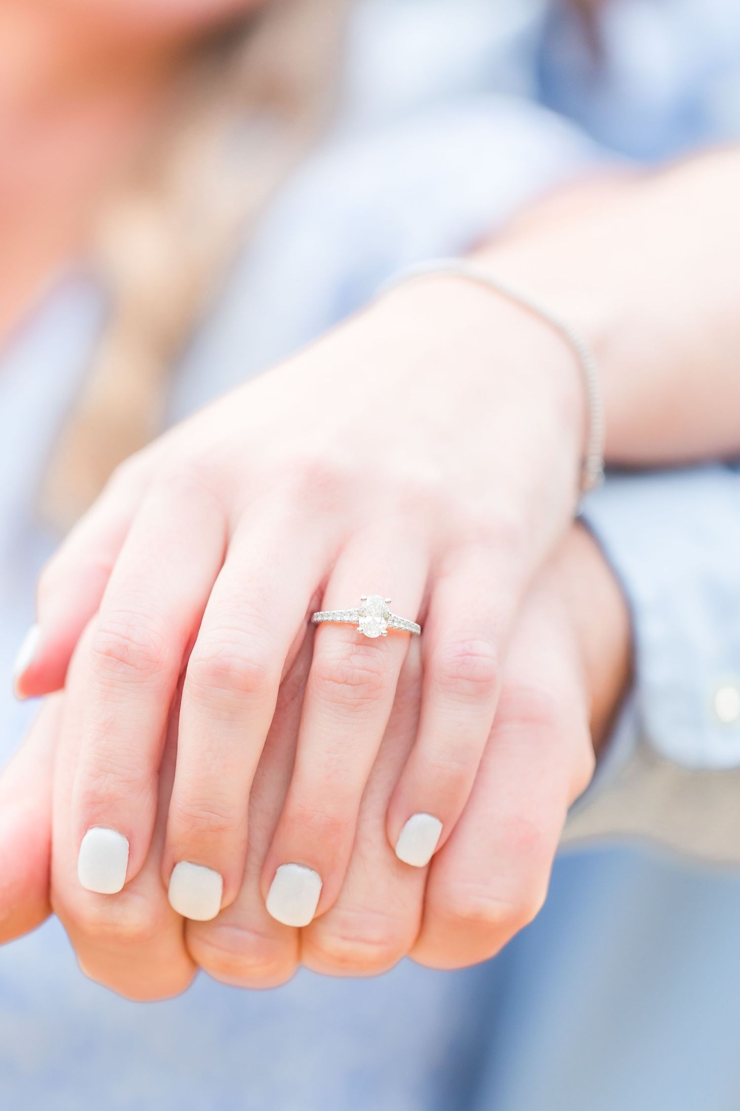 Close-up of hands showing off an engagement ring with white nail polish.
