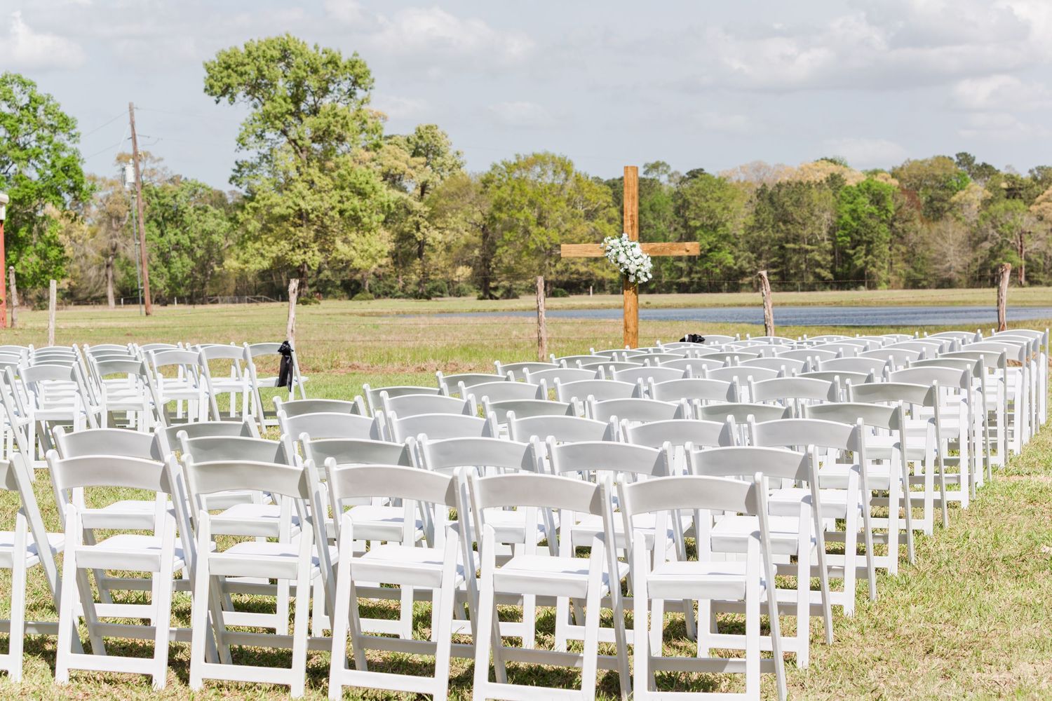 Rows of white wedding ceremony chairs set up in an open field with flags flying.