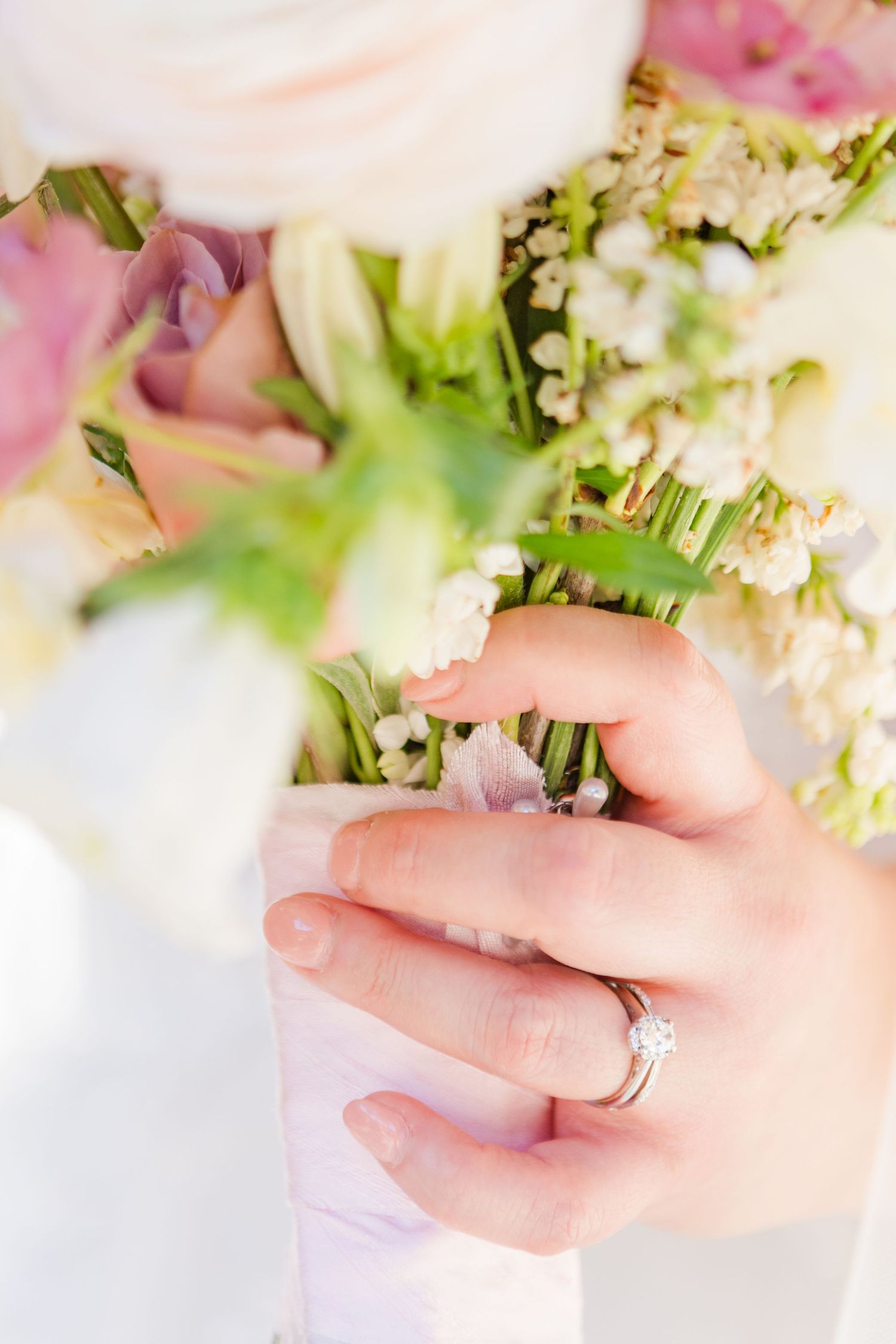 Close-up detail of delicate wedding bouquet being held with engagement ring visible.