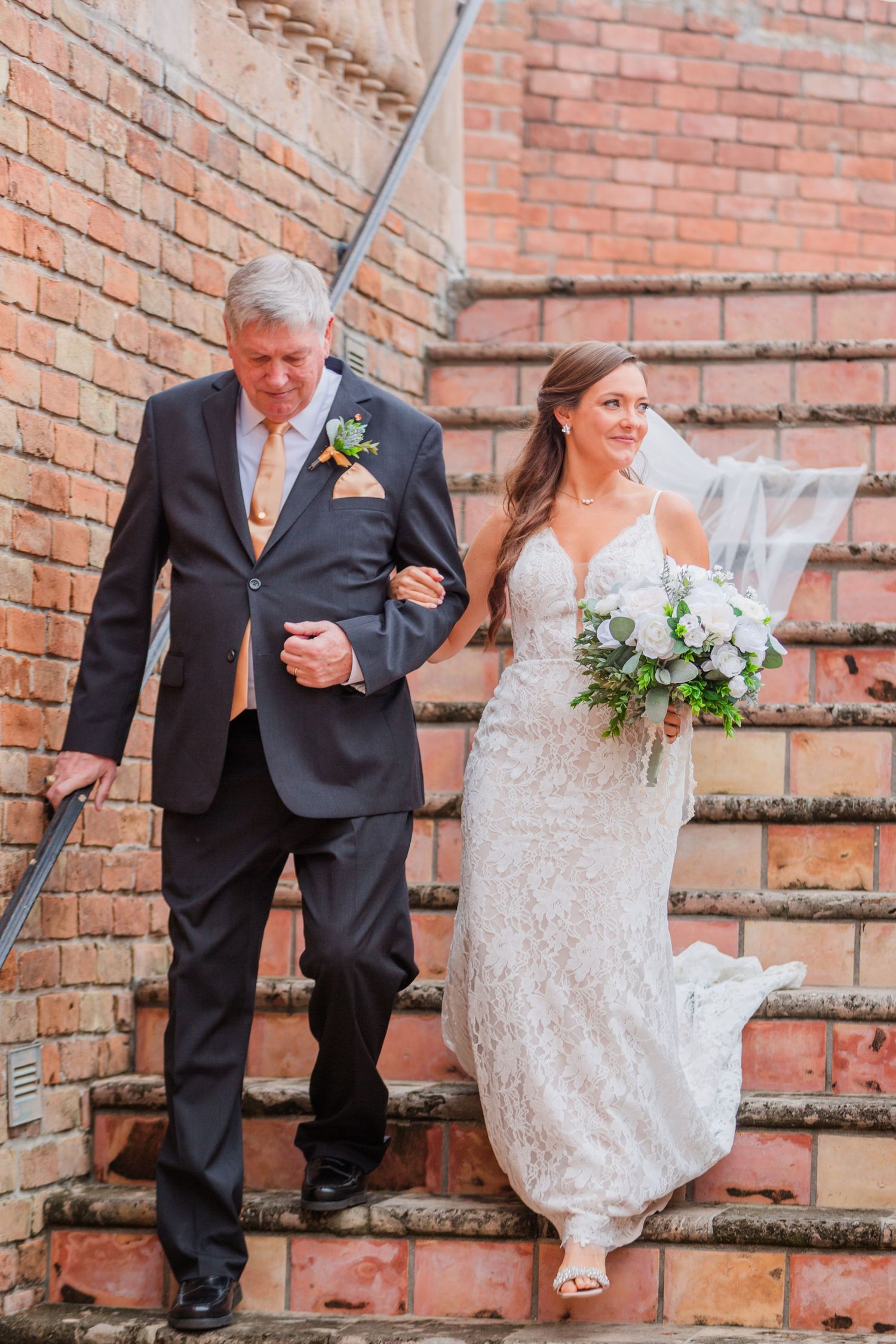Wedding party poses on brick steps in formal attire.