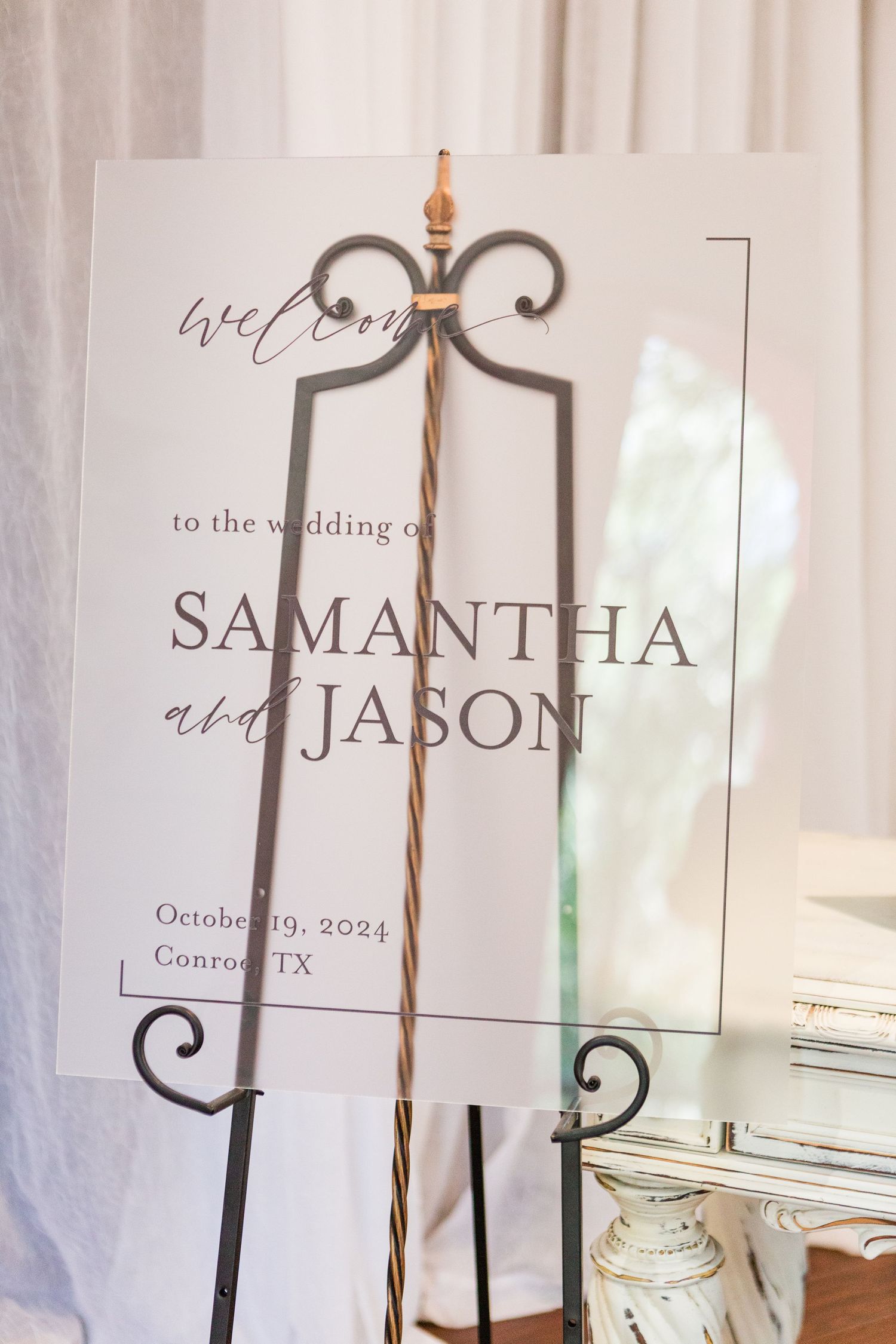 Elegant wedding welcome sign with calligraphy text displayed on a white stand with candle accents.