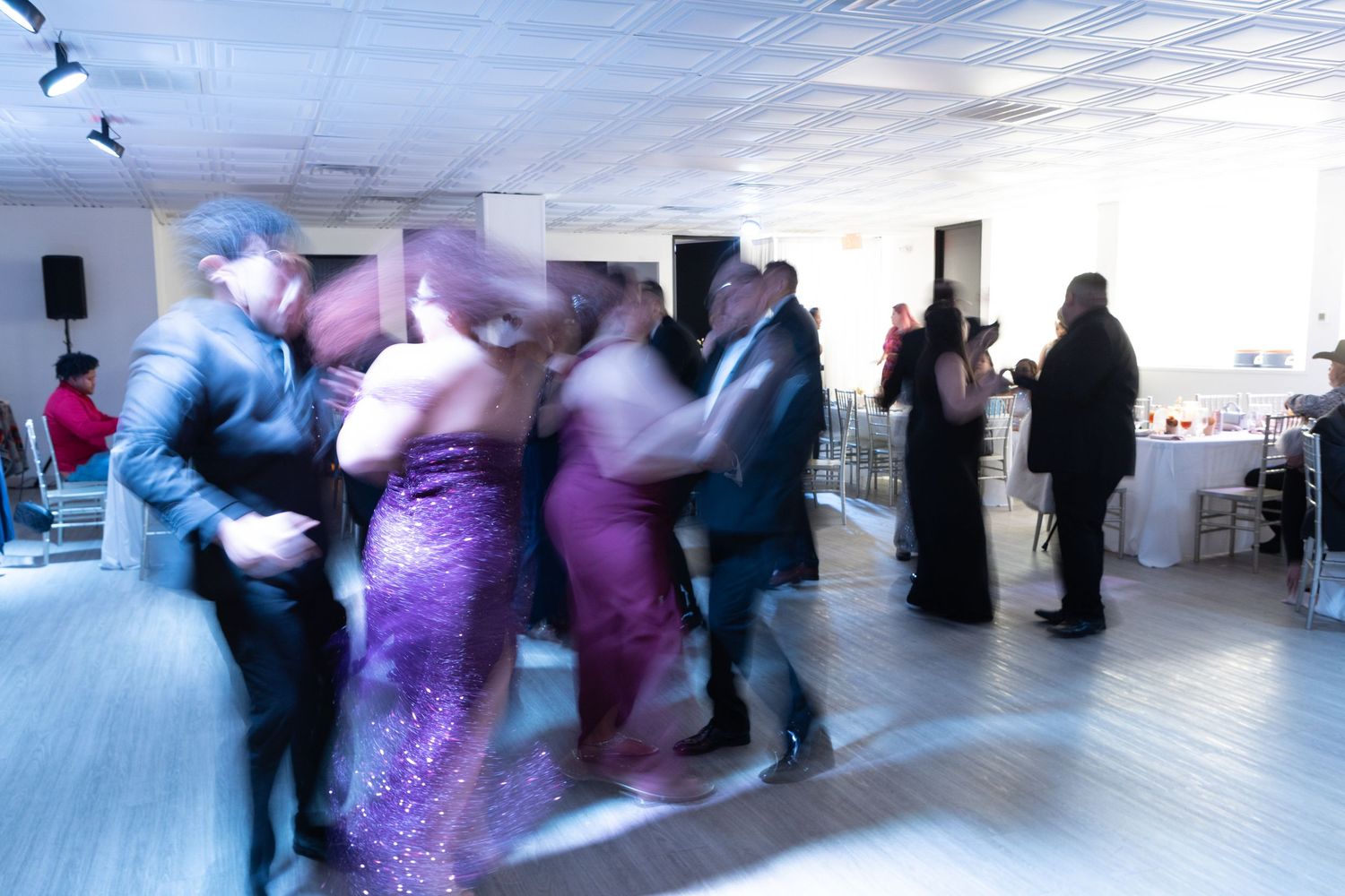 Blurred figures dancing energetically in formal wear at an indoor event space.