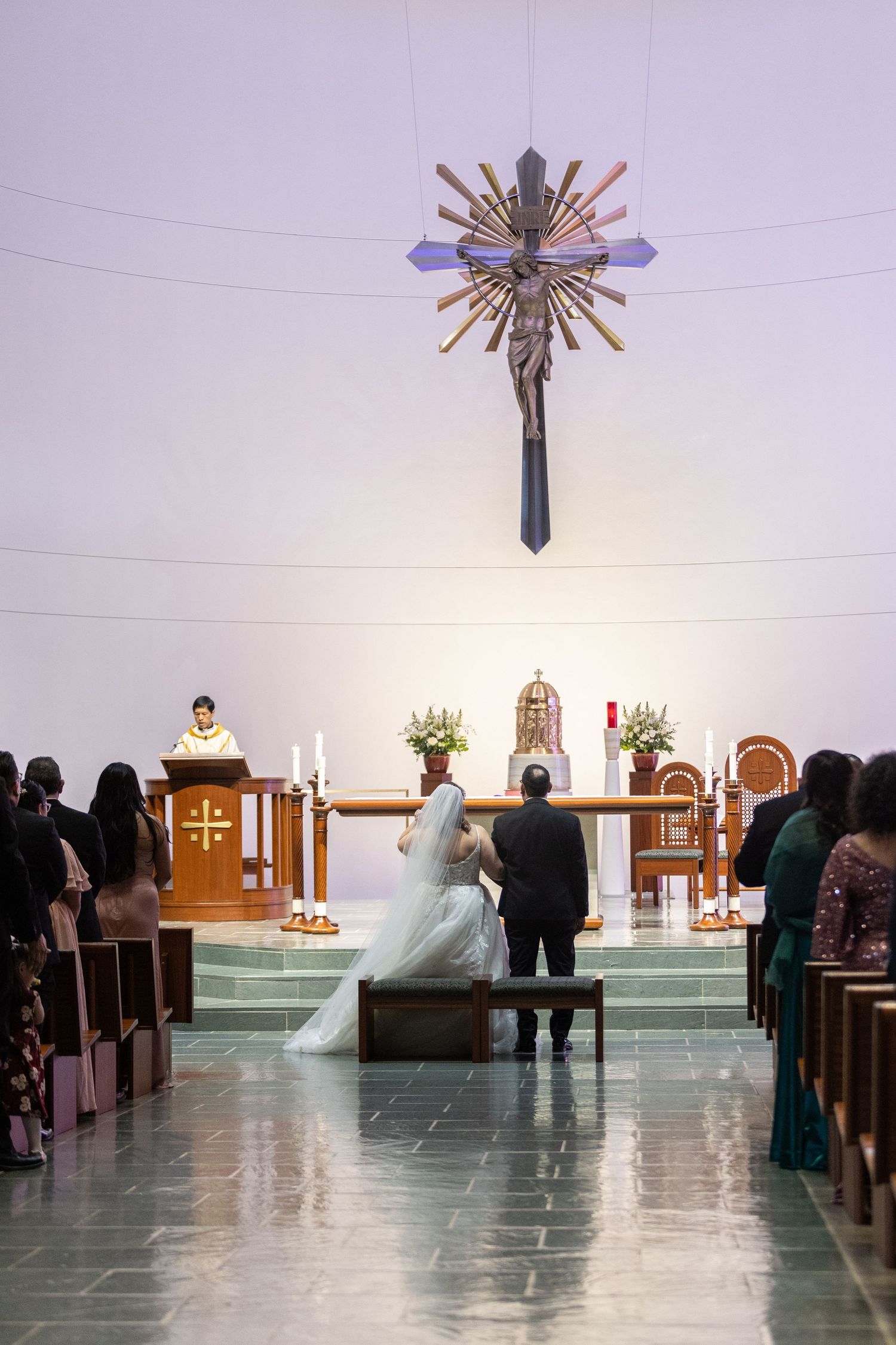 Wedding ceremony in progress inside a contemporary church with distinctive lighting fixtures.