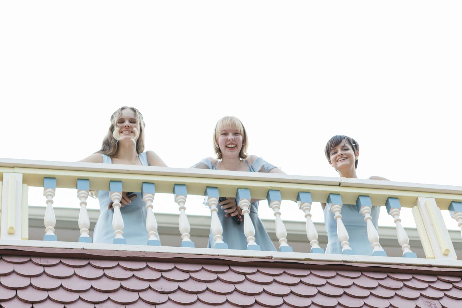 People watching from balcony of Victorian-style house during event.