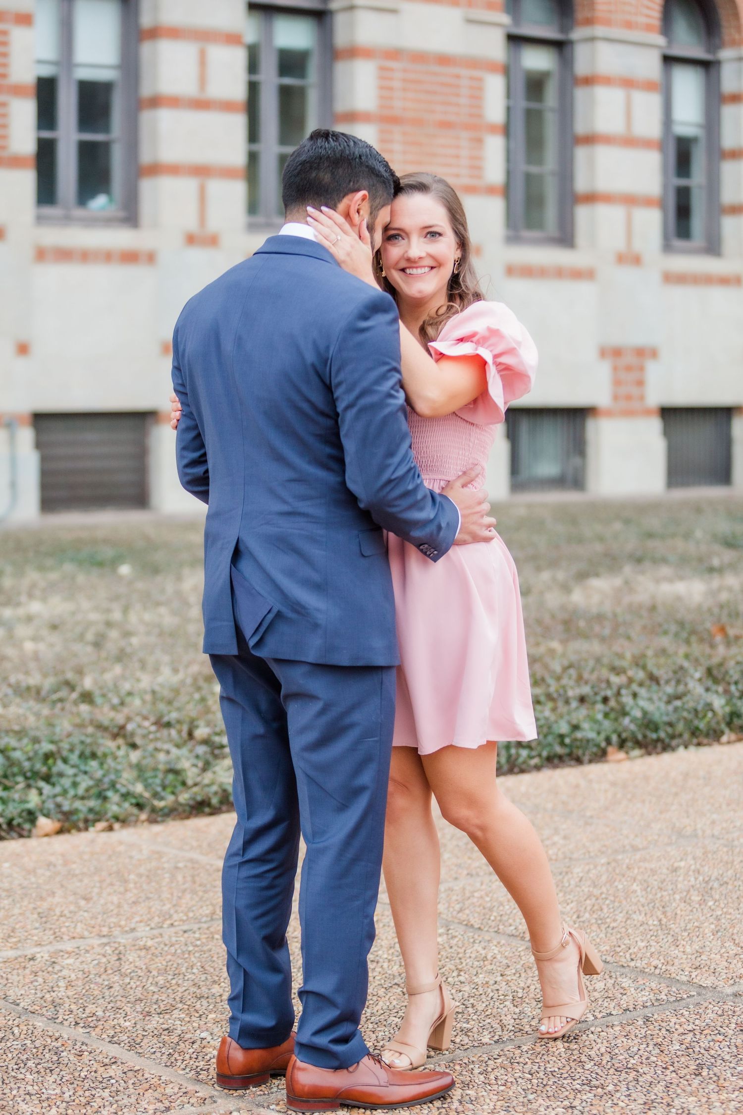 Couple sharing an intimate moment against white stone building with decorative brick accents.