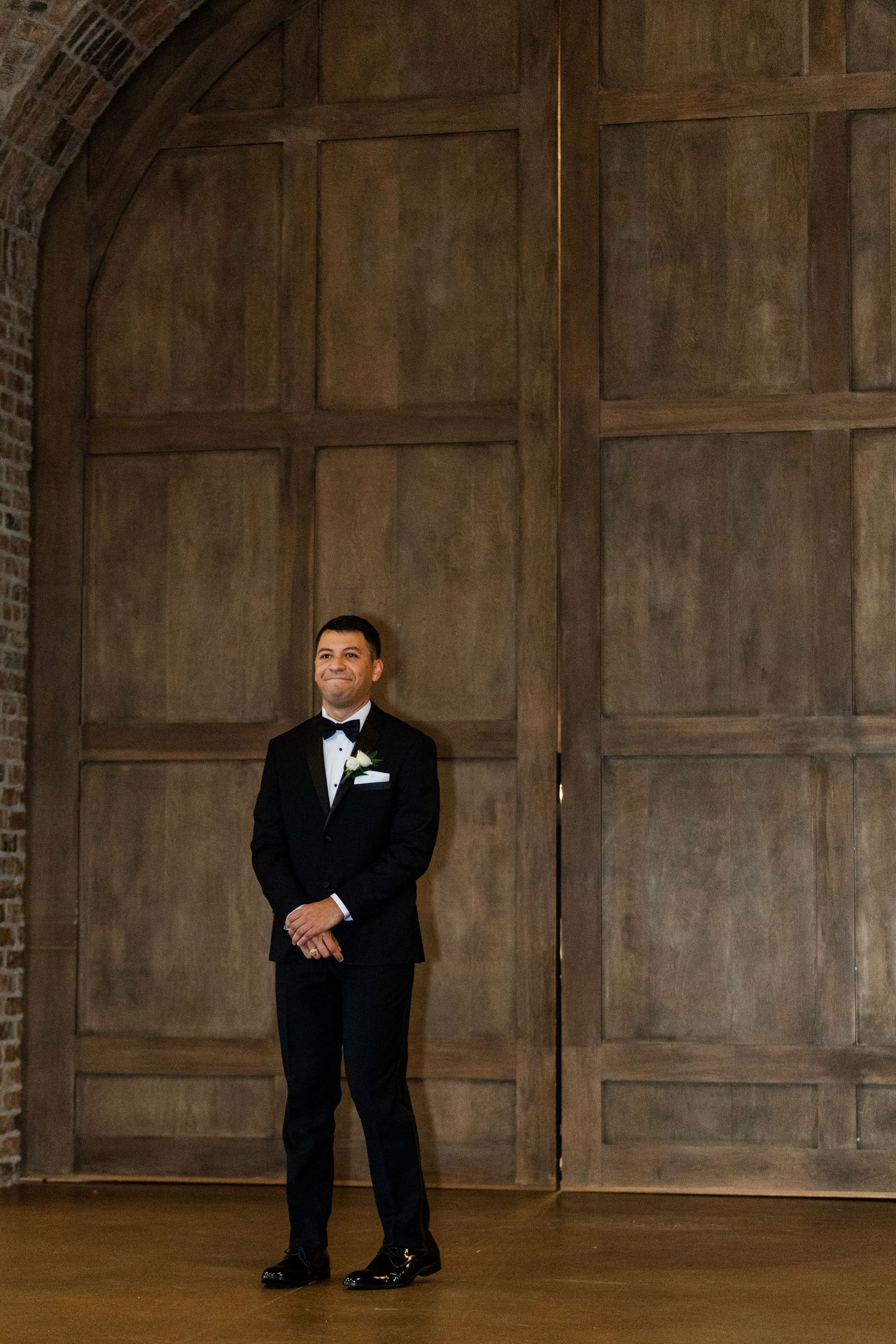 Stylish groom poses against rustic wooden panels in a modern venue setting.