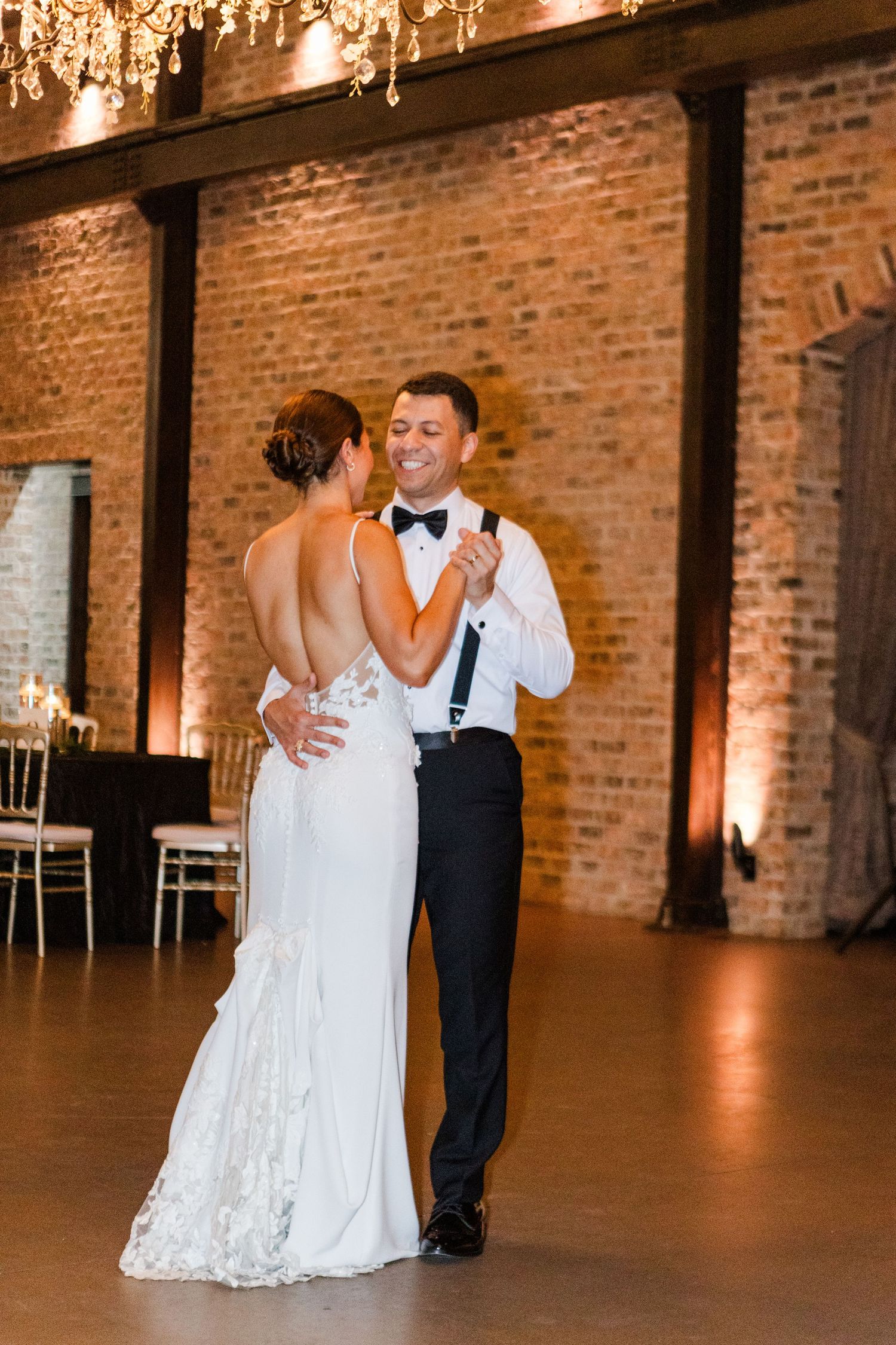 Classic wedding dance in elegant brick-walled venue with warm lighting.