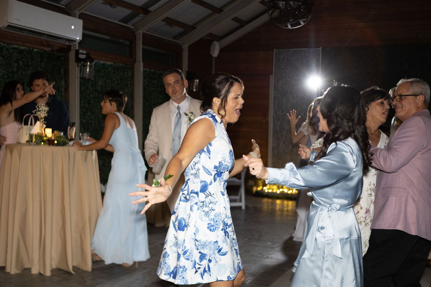Wedding party celebration with guests dancing in blue floral dresses at an evening reception.