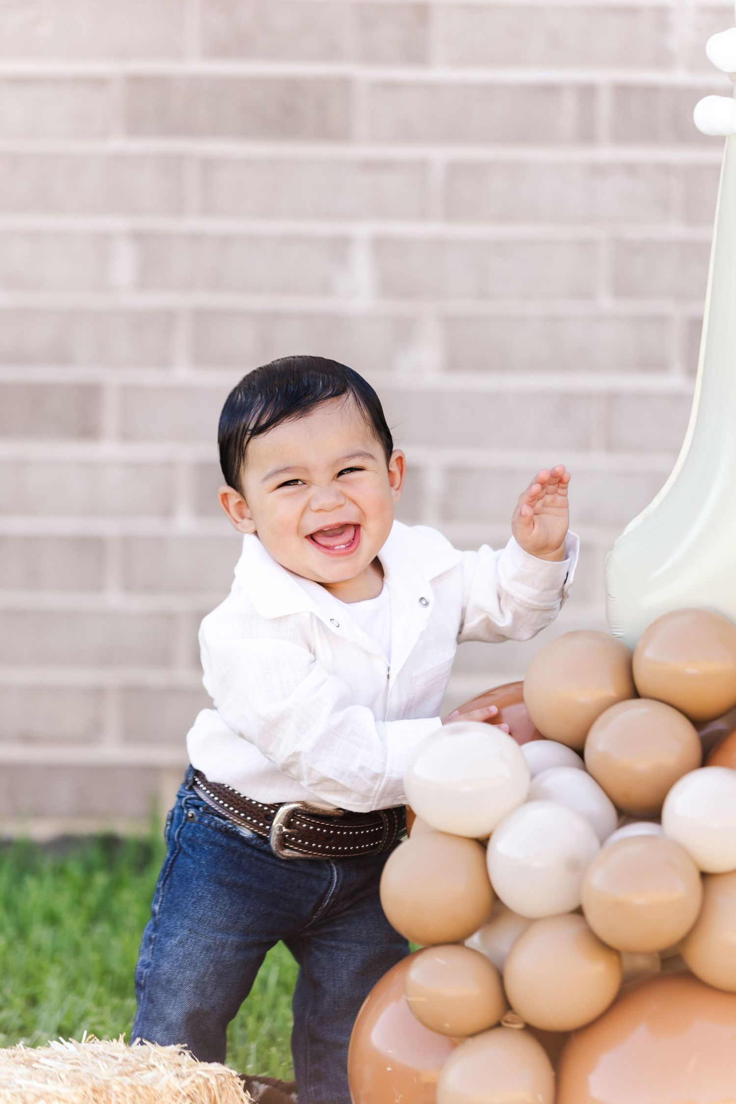 Happy child in white shirt and jeans plays near beige balloon decorations.