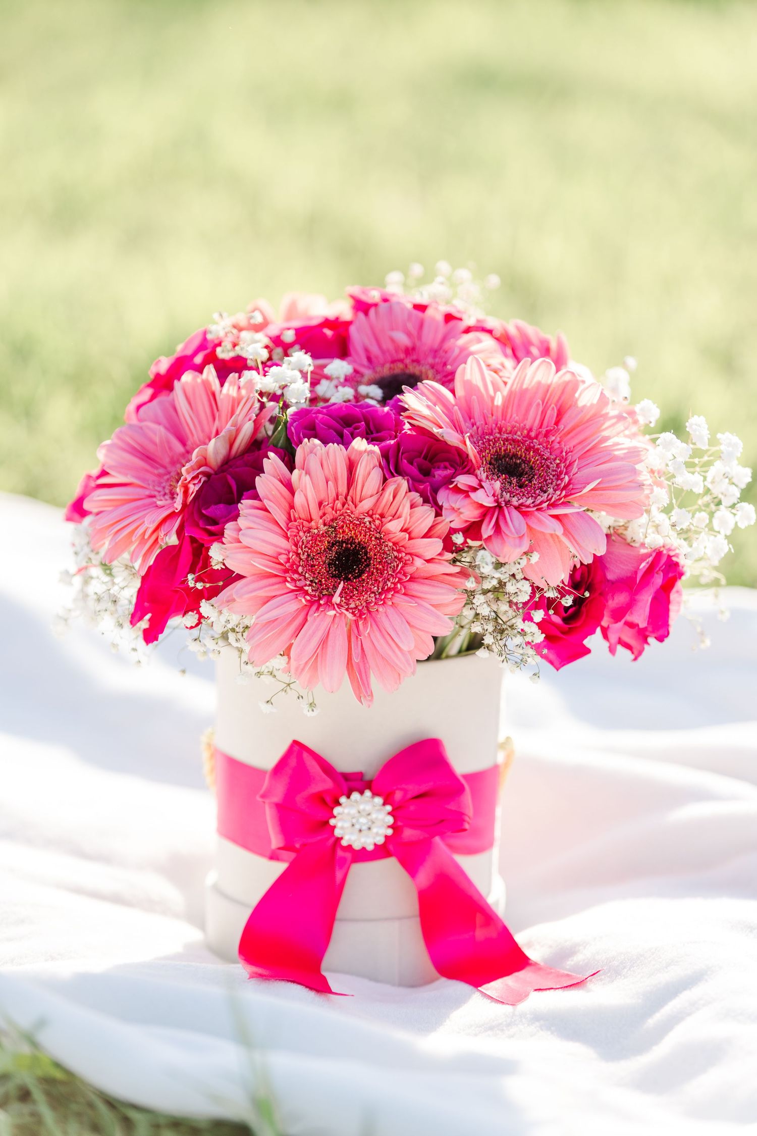 White vases filled with pink gerbera daisies and baby's breath decorated with hot pink bows.