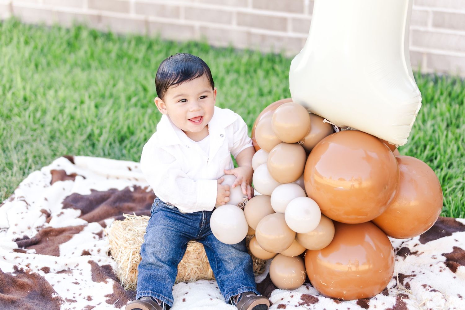 Child seated next to fall decorations and brown balloons against a brick wall backdrop.
