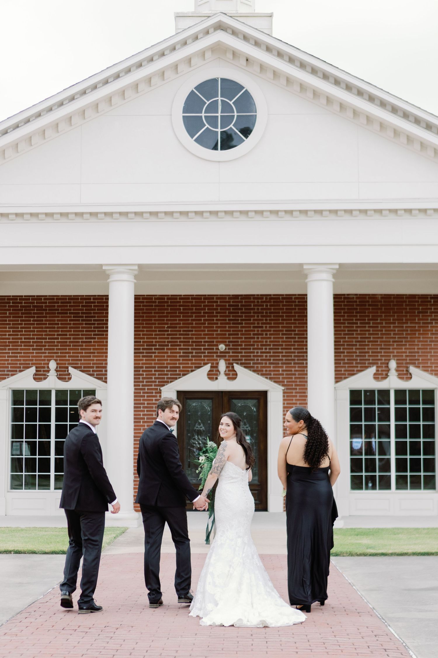 Wedding party poses outside classic white colonial building with brick and columns on wedding day.