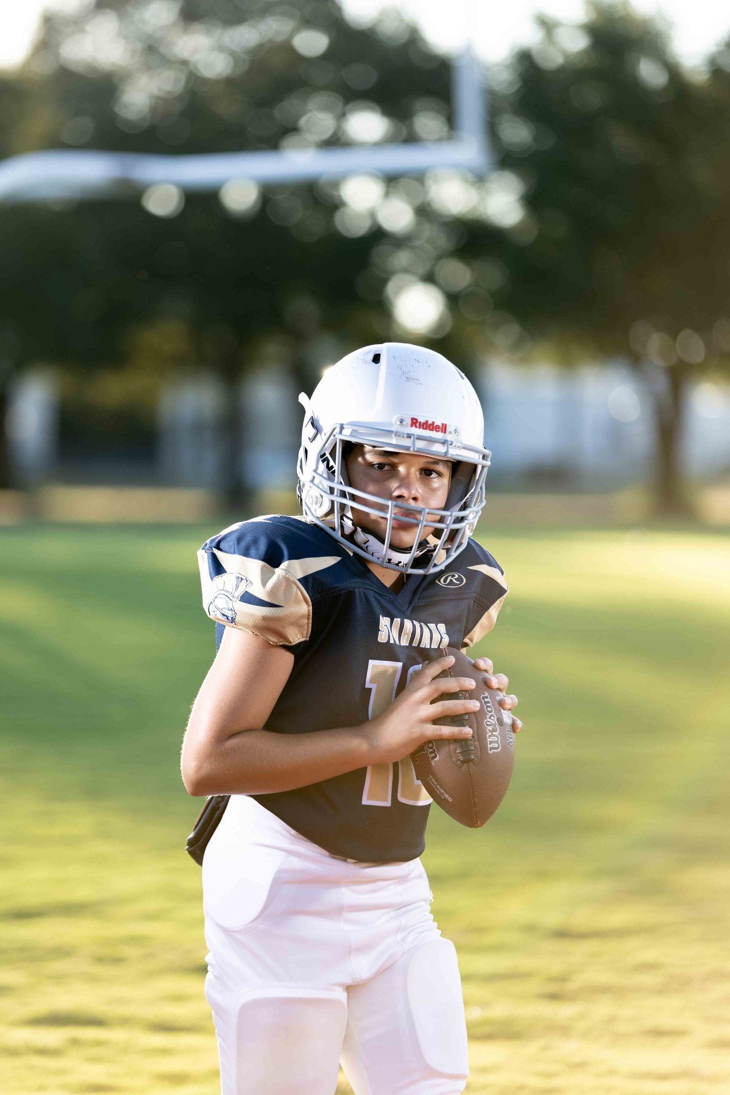 Football player in white jersey and black helmet practices catching techniques on sunny field during training session.