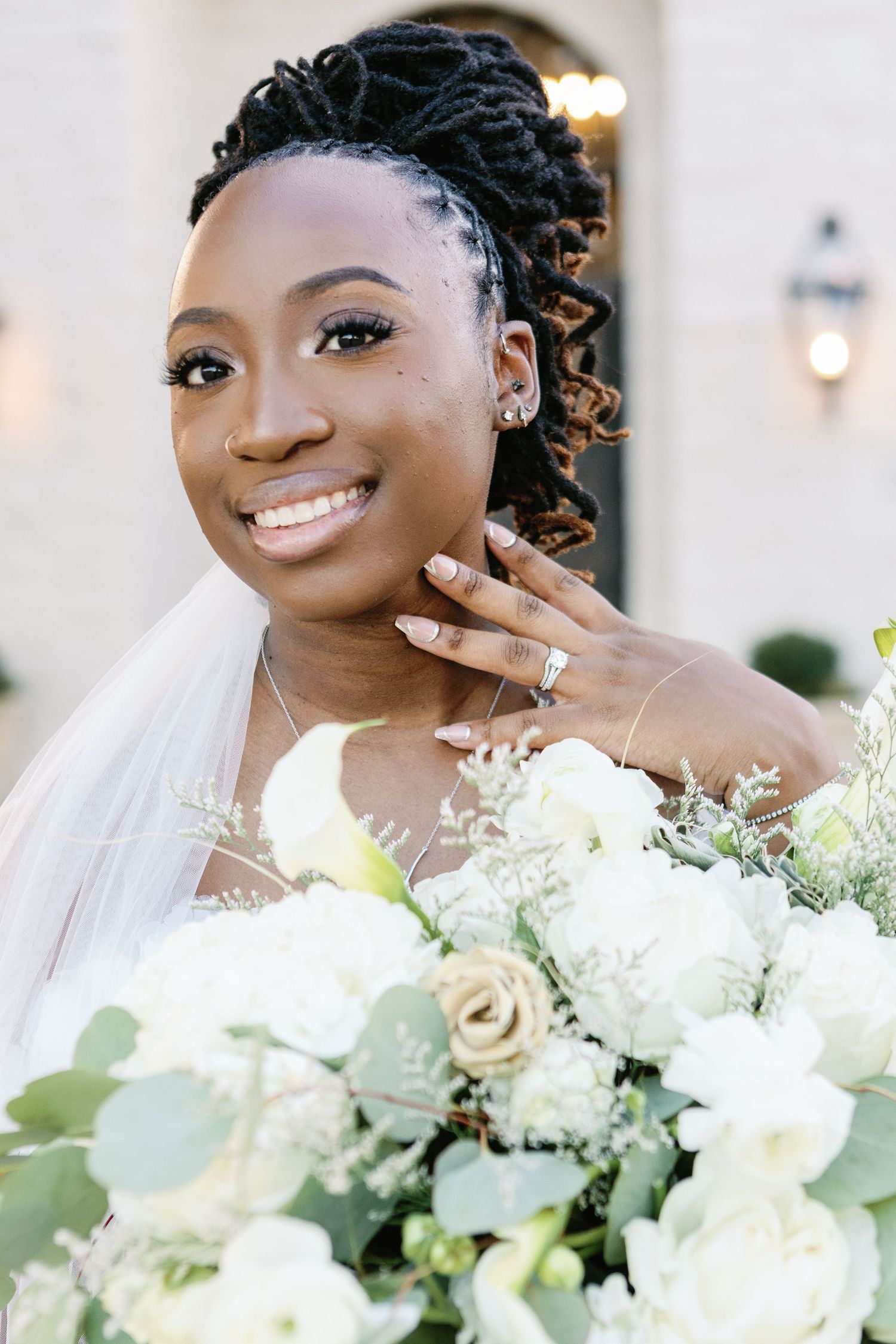 Beautiful bridal portrait featuring an elegant white bouquet with roses and greenery against a light background.