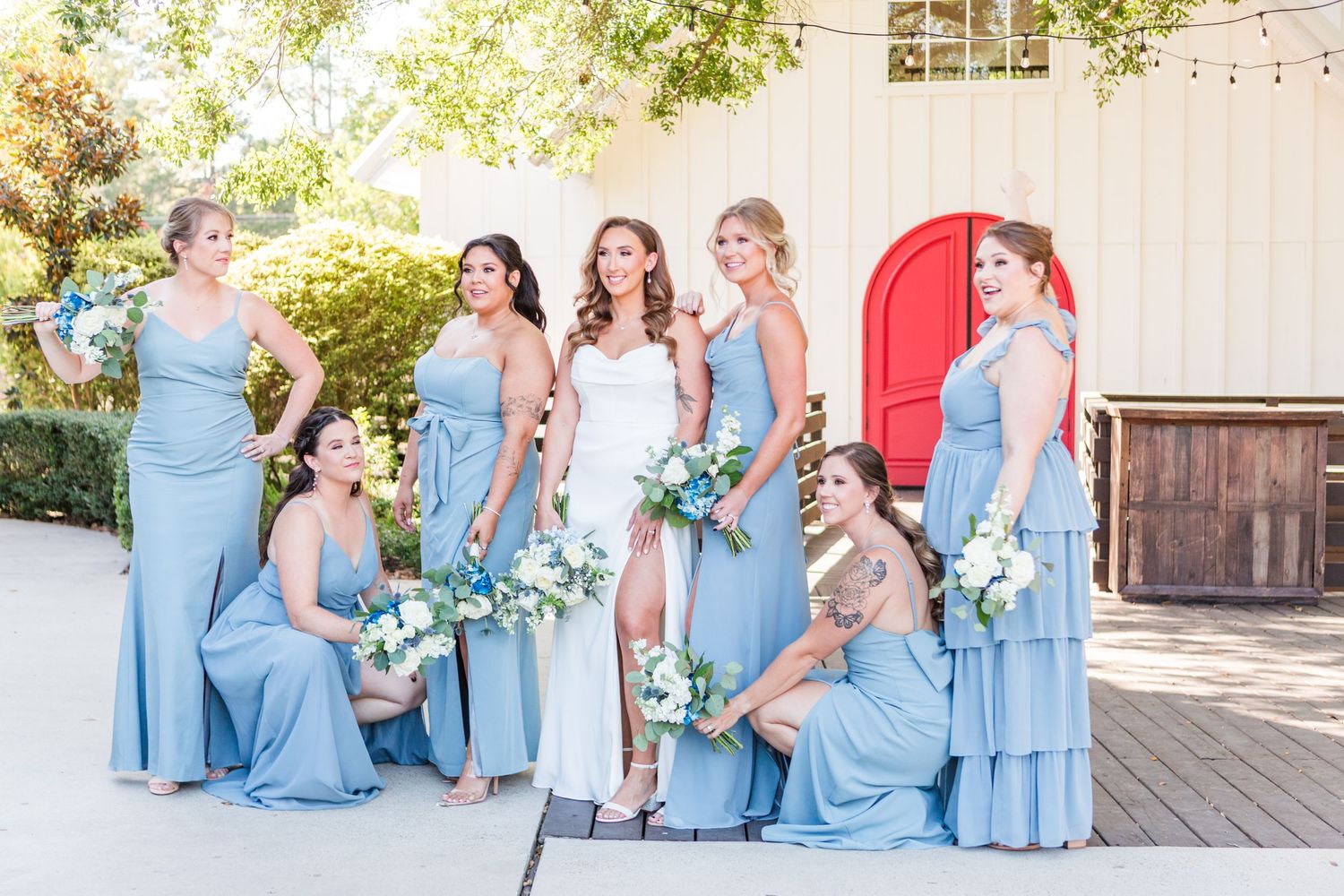 Wedding party wearing light blue dresses poses in front of white building with red door.
