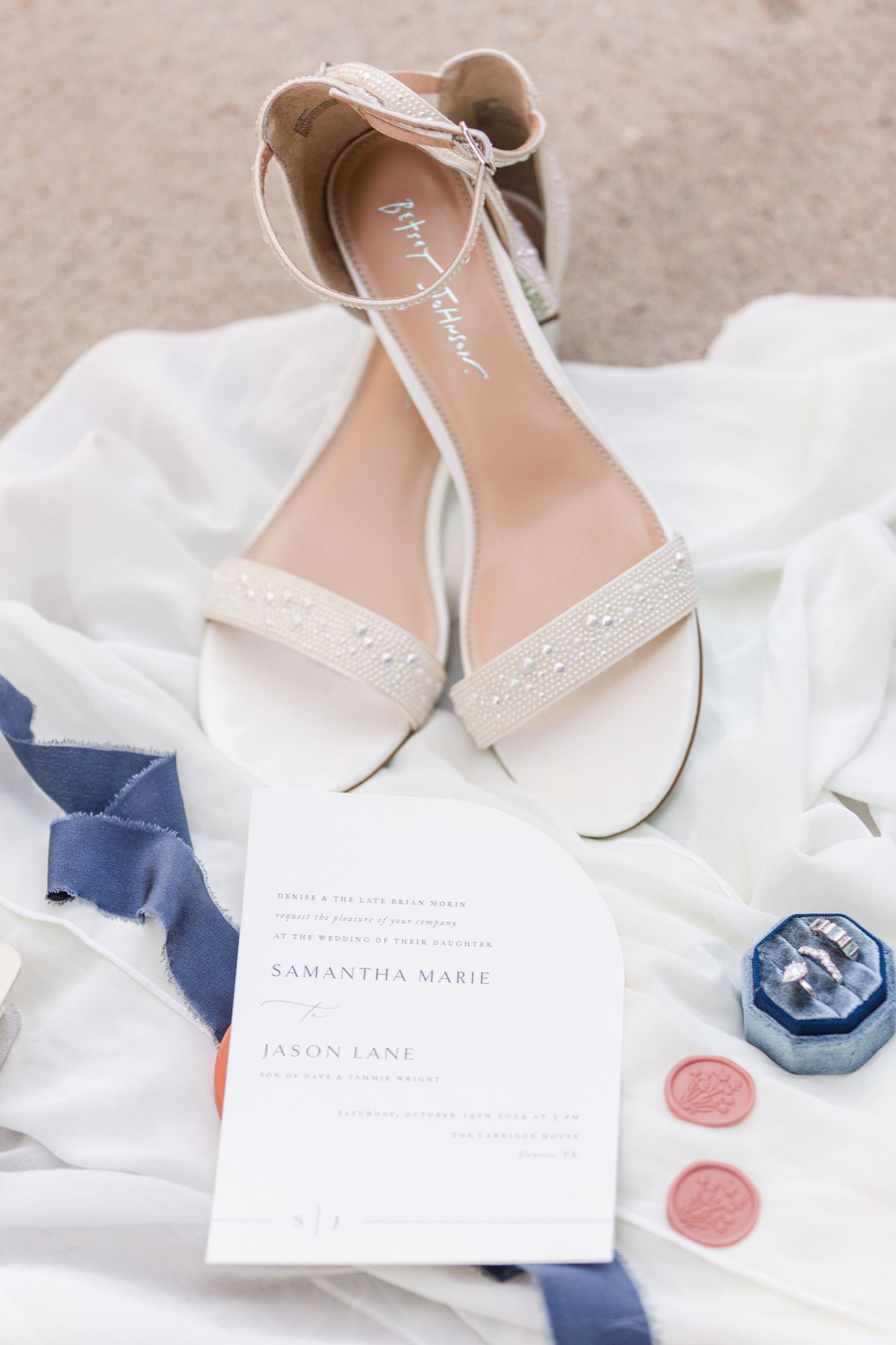Wedding shoes and stationery styled with navy and pink wax seals on white fabric.