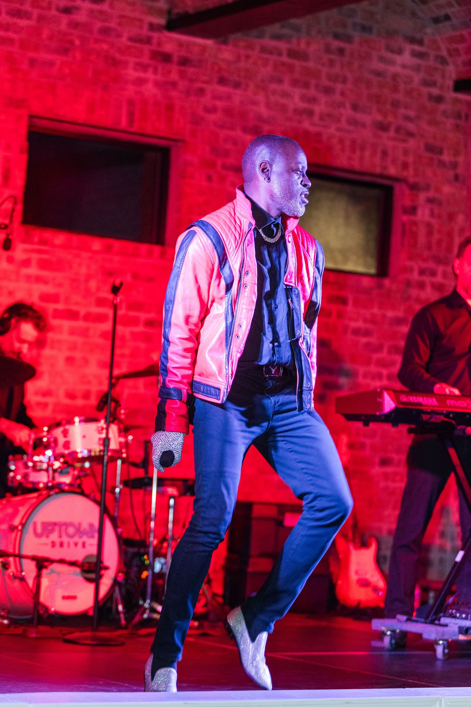 Dynamic performance with red lighting illuminates brick walls as dancer moves across stage.