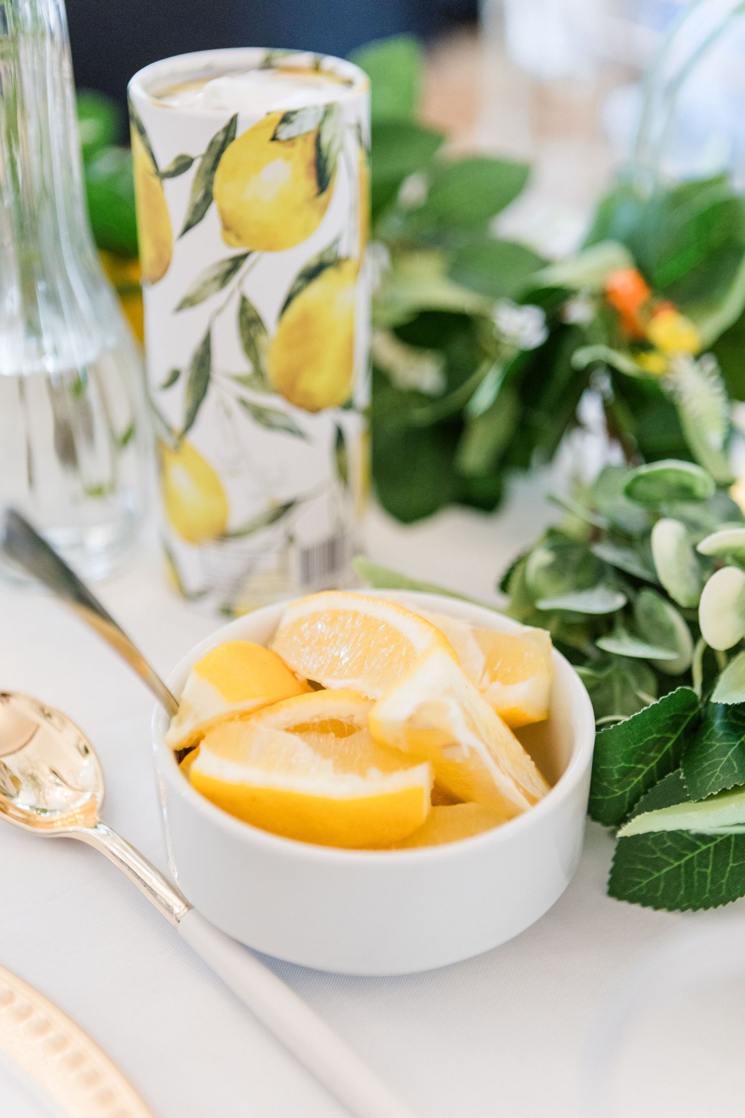 Fresh citrus slices and greenery decorate white table settings with lemon-patterned glassware.