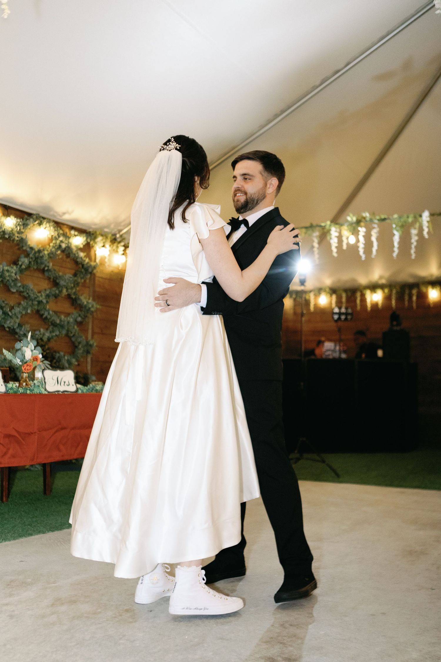 A couple in wedding attire performs a romantic dance sequence in a ballroom with greenery decorations.