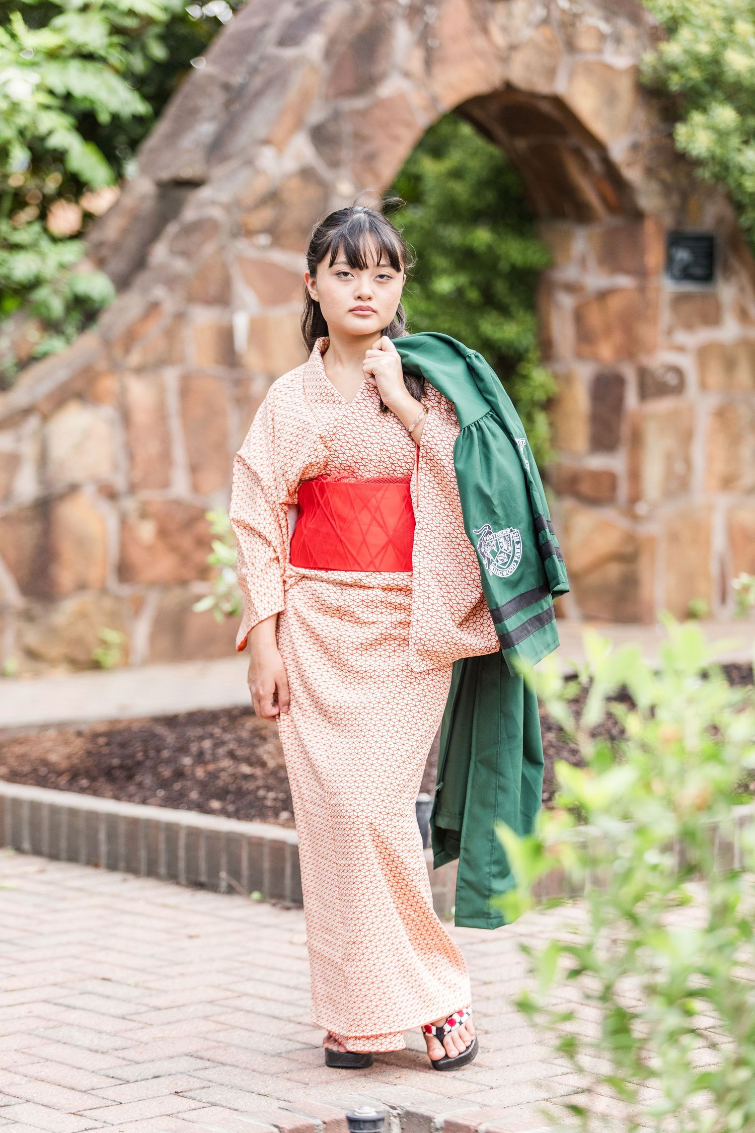Person wearing orange and white patterned kimono and green accessories on stone pathway.