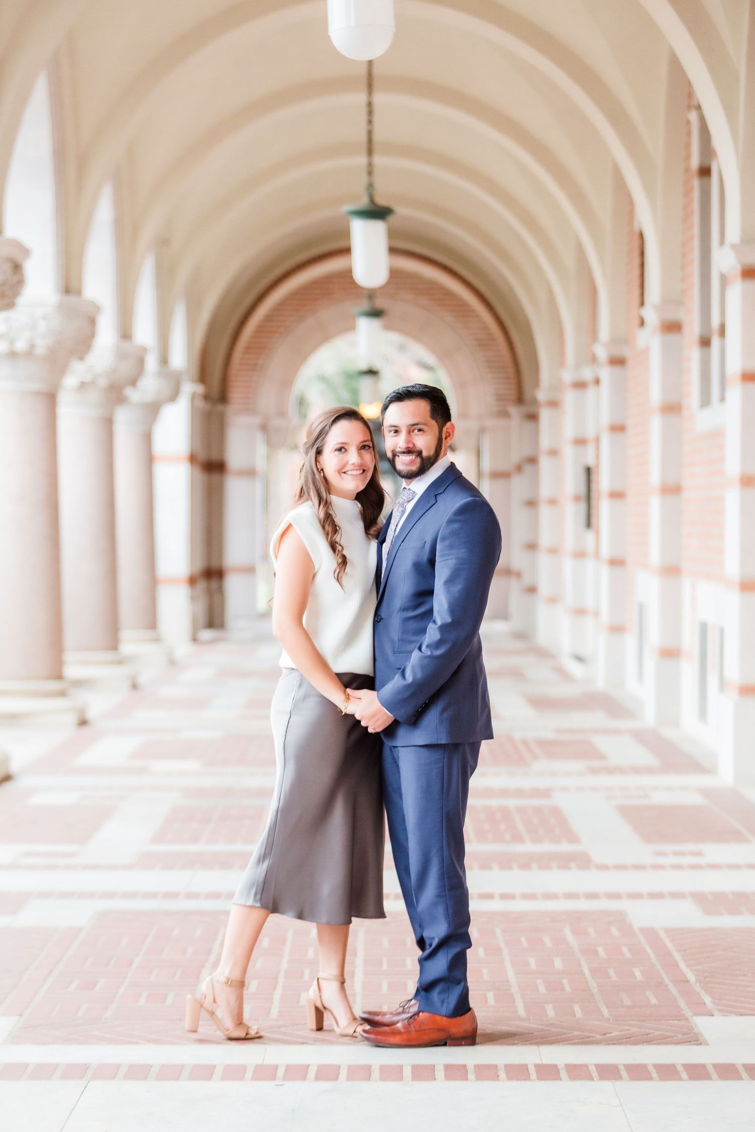 Formal portrait in bright hallway with repeating arches and columns.