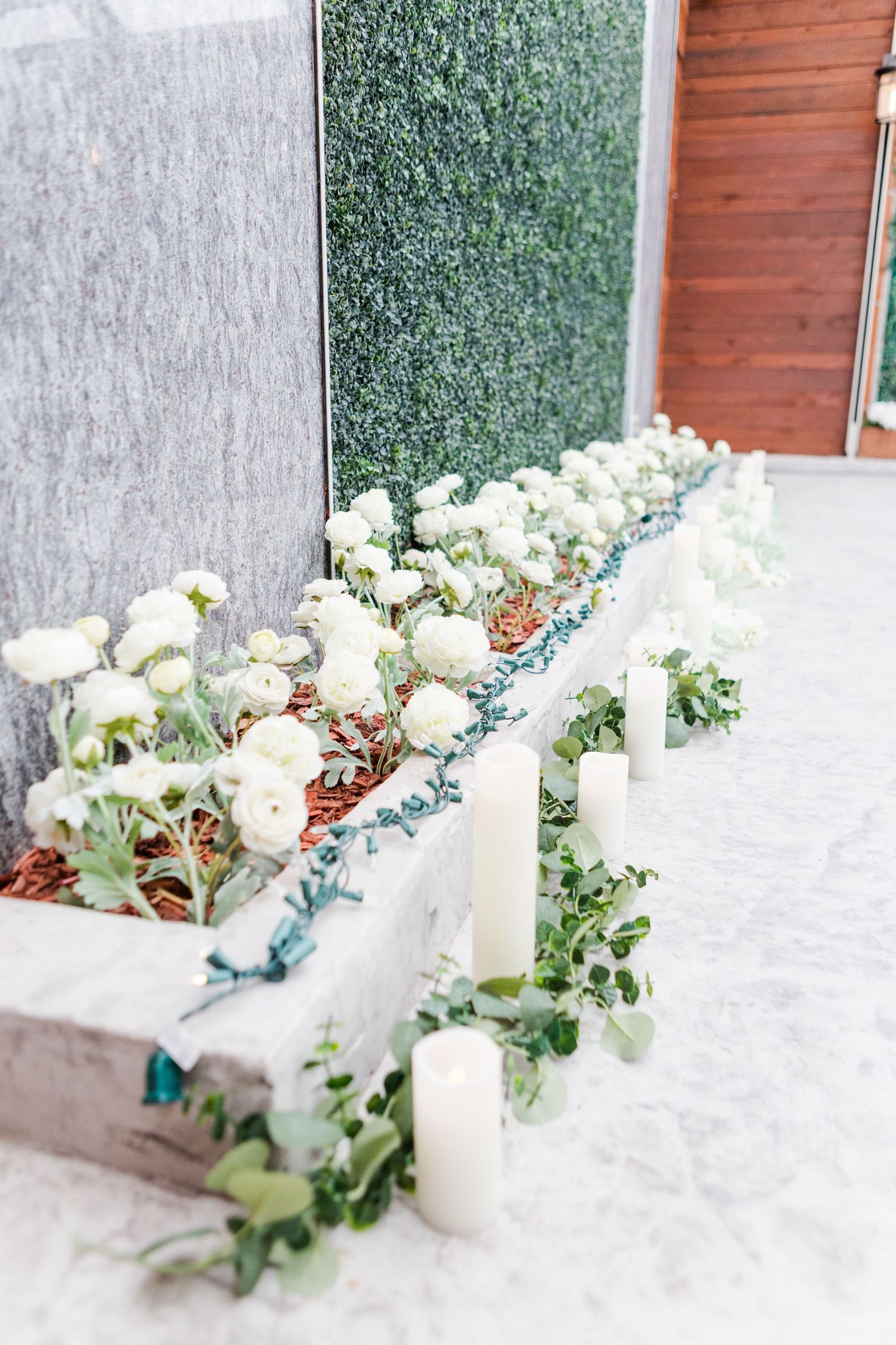 White floral centerpiece with candles and greenery arranged on a textured surface.