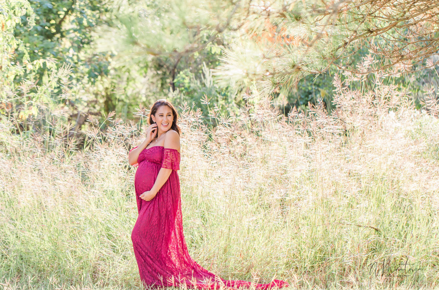 Woman in flowing red dress poses gracefully in golden sunlit field during photo session.