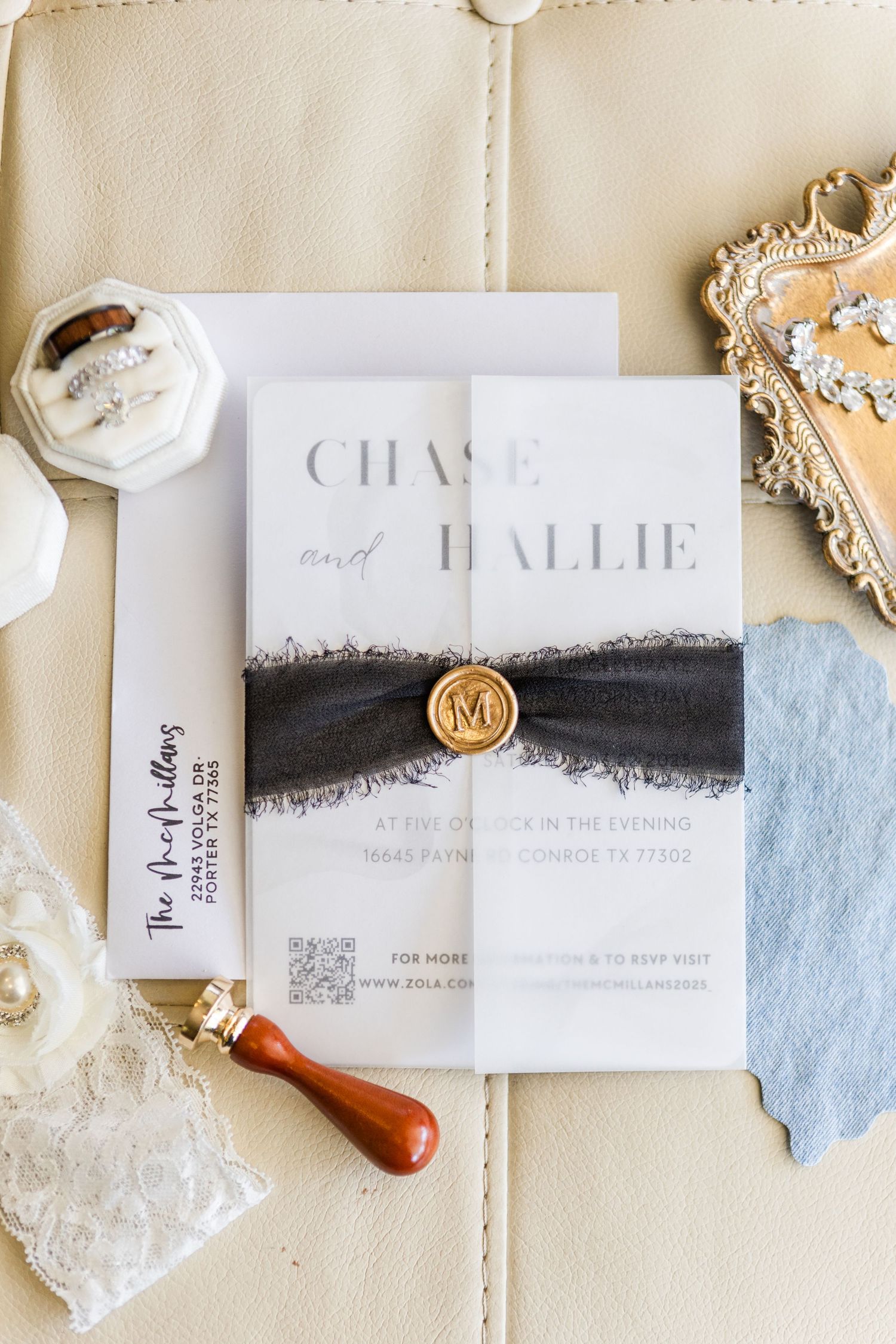 Elegant wedding invitation with black ribbon band and gold wax seal on cream background.