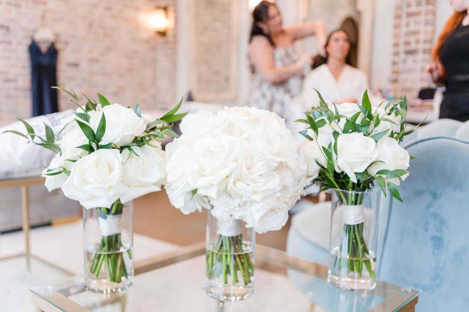 Beautiful white floral centerpieces with roses and greenery line the wedding reception tables.