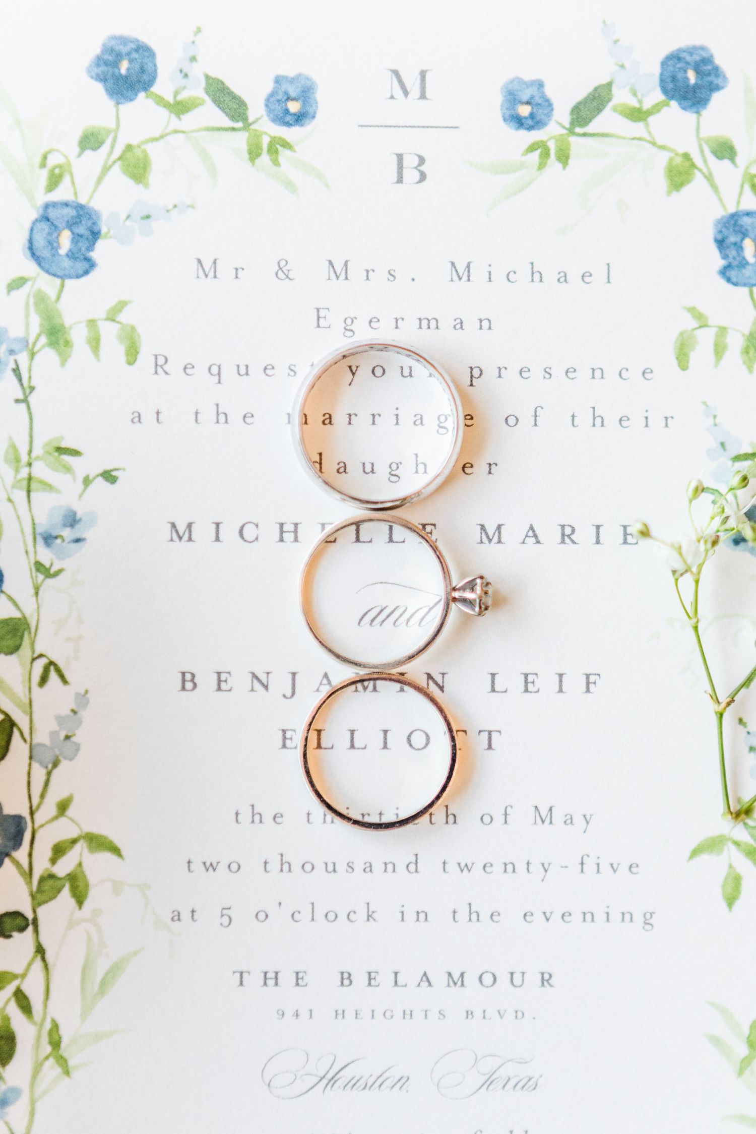 Wedding invitation and rings styled with soft blue floral design elements.