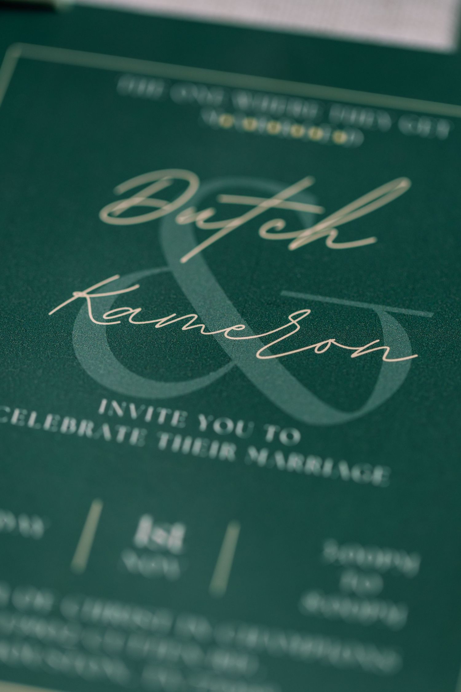 Close-up view of elegant wedding invitation text in white calligraphy on emerald green paper.