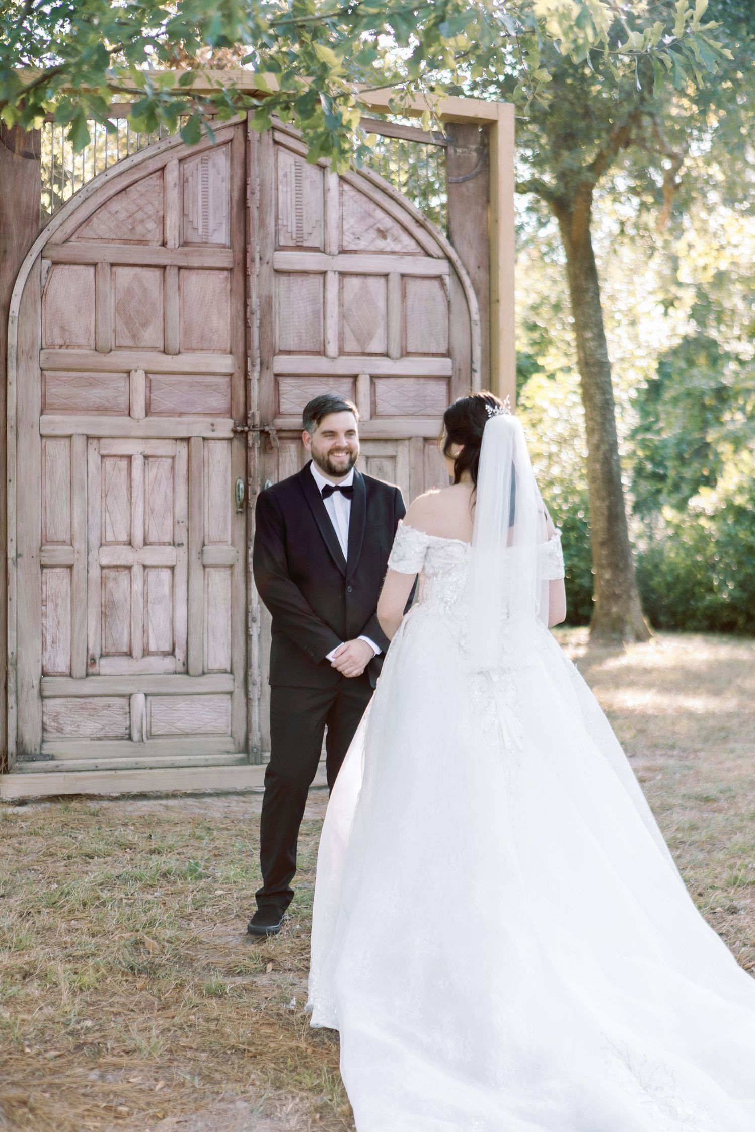 Romantic first look wedding photos captured in front of rustic pink doors in a garden setting.