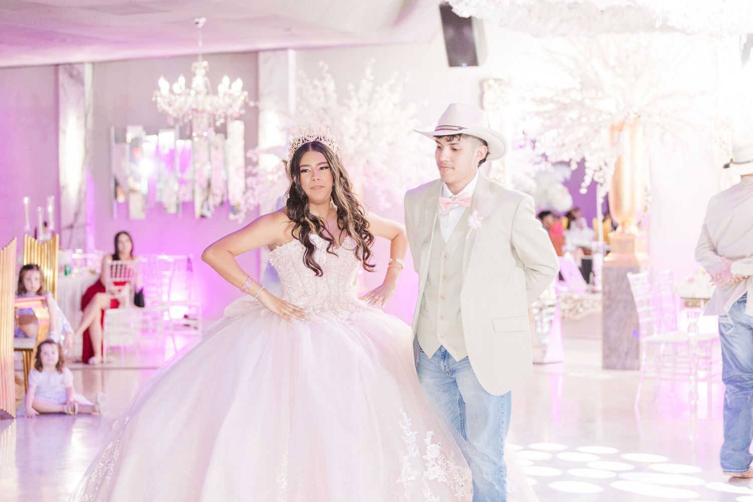 Elegant pose in a light pink quinceañera gown against a backdrop of white floral decorations.