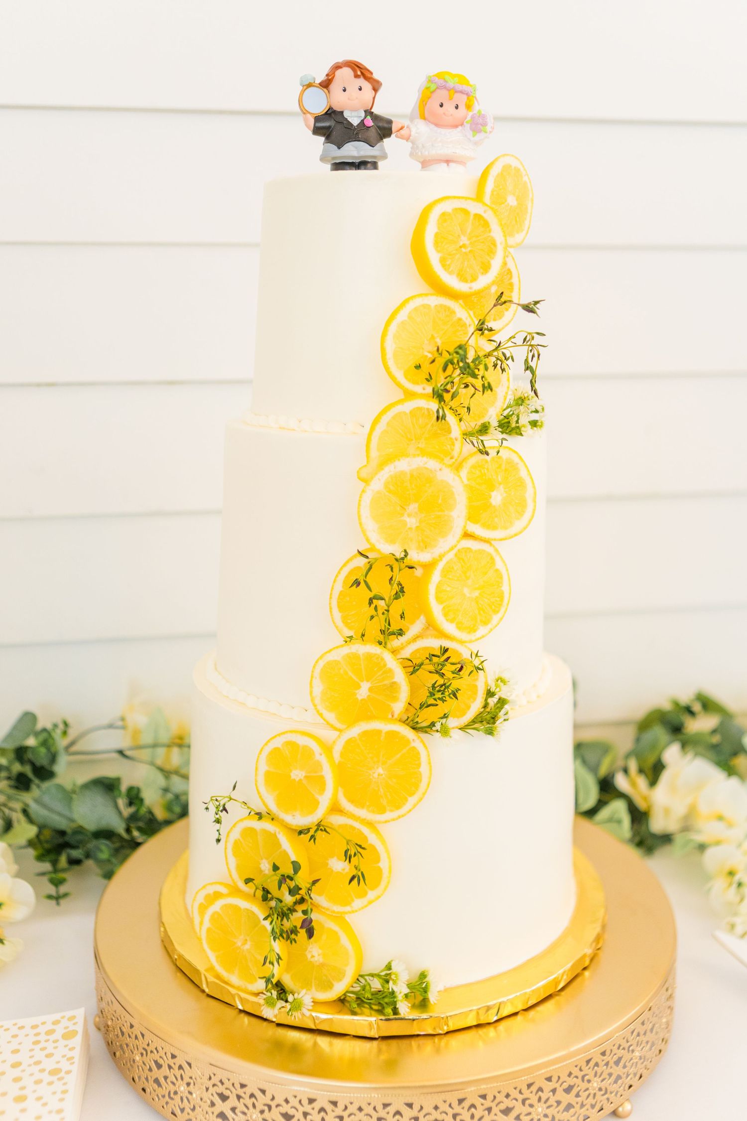 White wedding cake decorated with fresh orange slices and herbs on a gold cake stand.