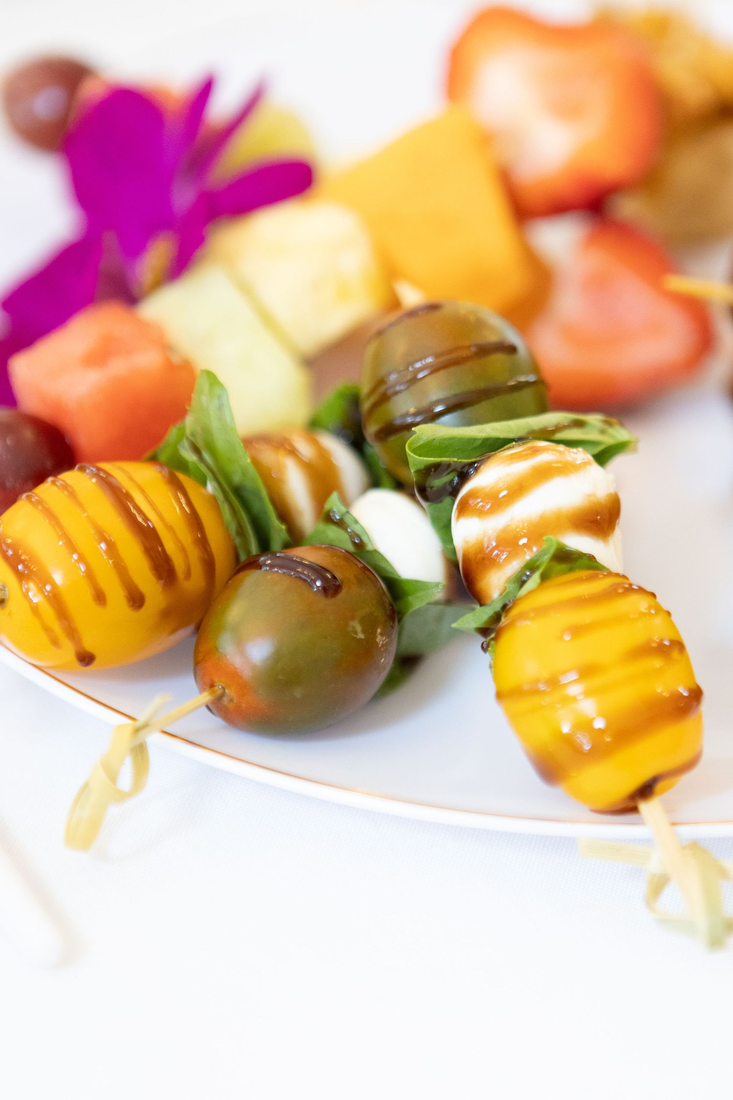 Vibrant appetizer skewers with grilled pineapple, tomatoes, and colorful garnishes arranged on white plates.