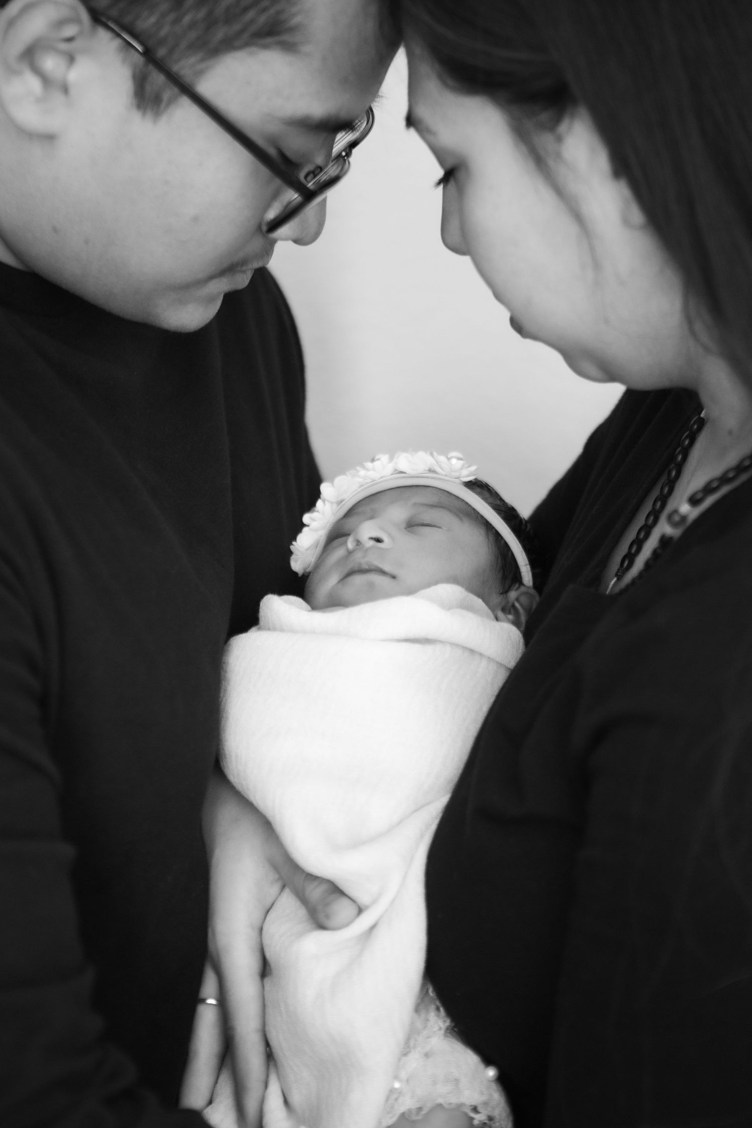 Black and white portraits of new parents tenderly cradling their swaddled newborn.