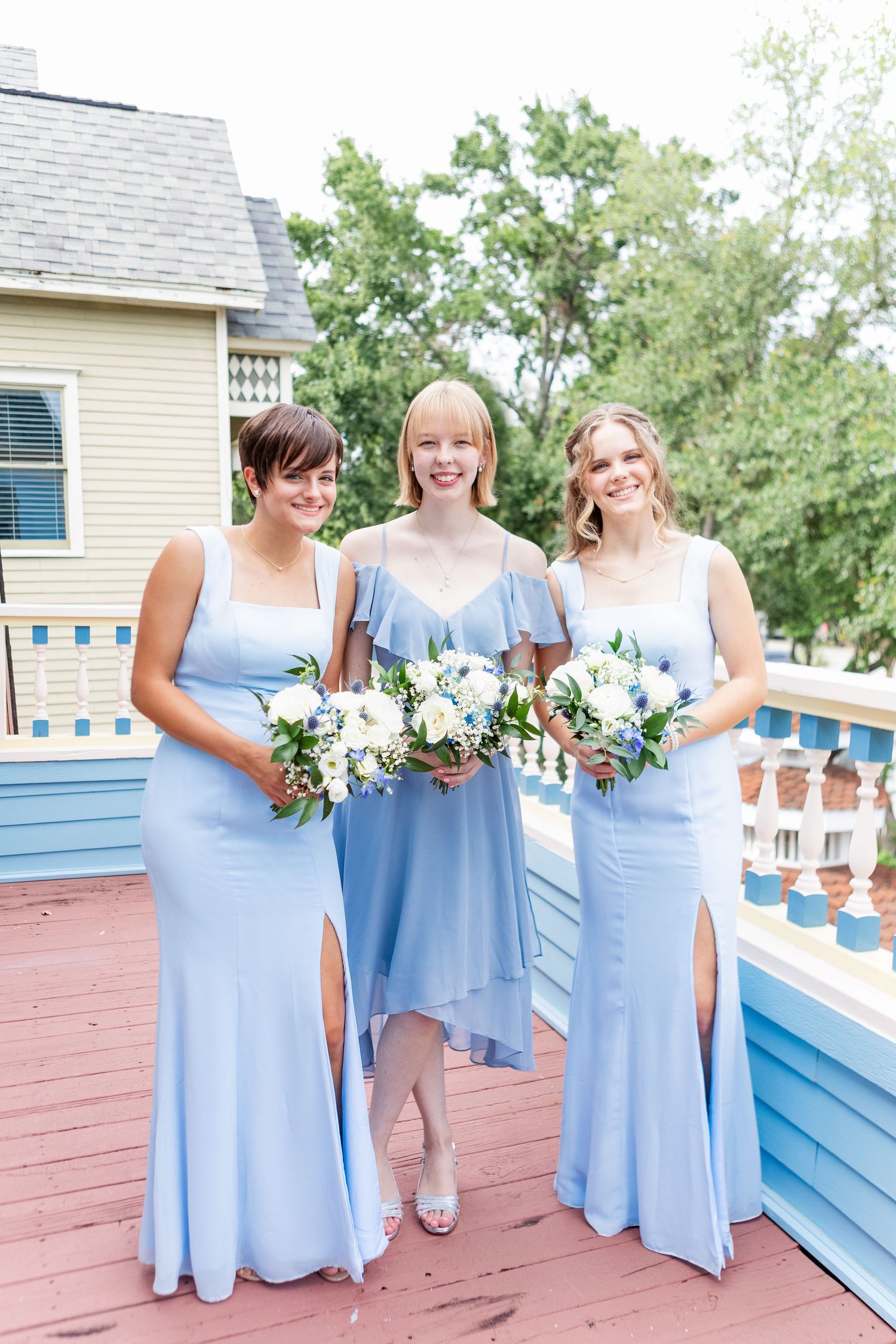 Bridesmaids in powder blue dresses holding white bouquets on outdoor deck.