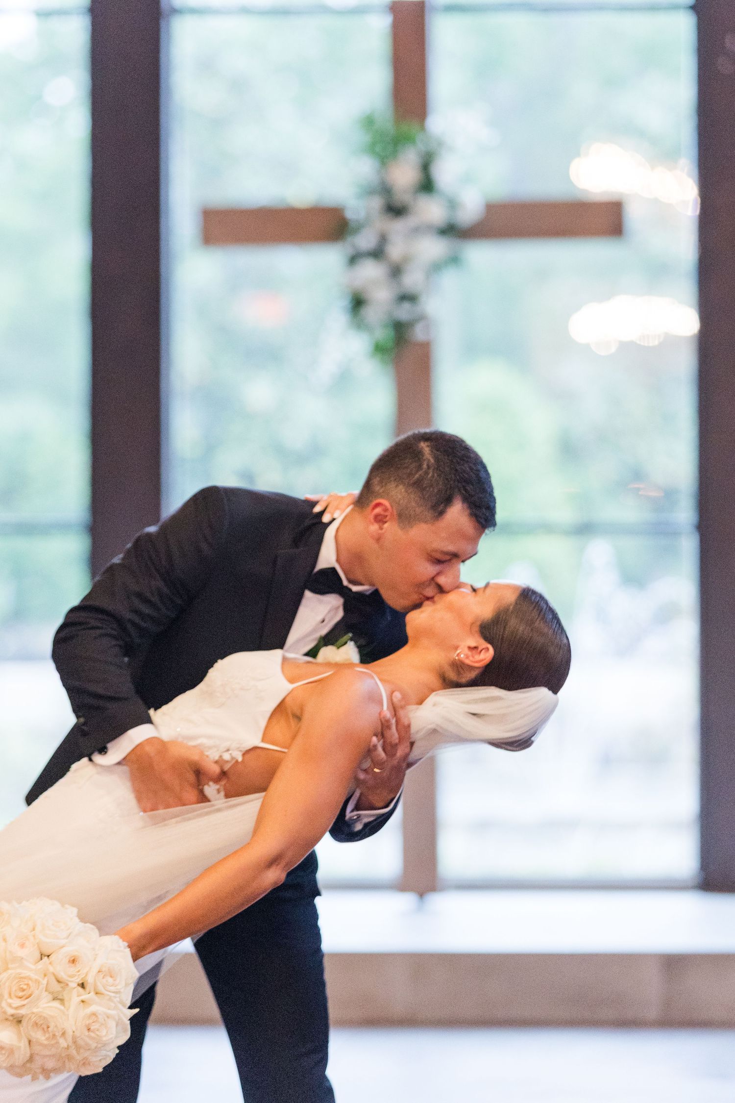 A romantic dip kiss between newlyweds in a sunlit wedding venue.